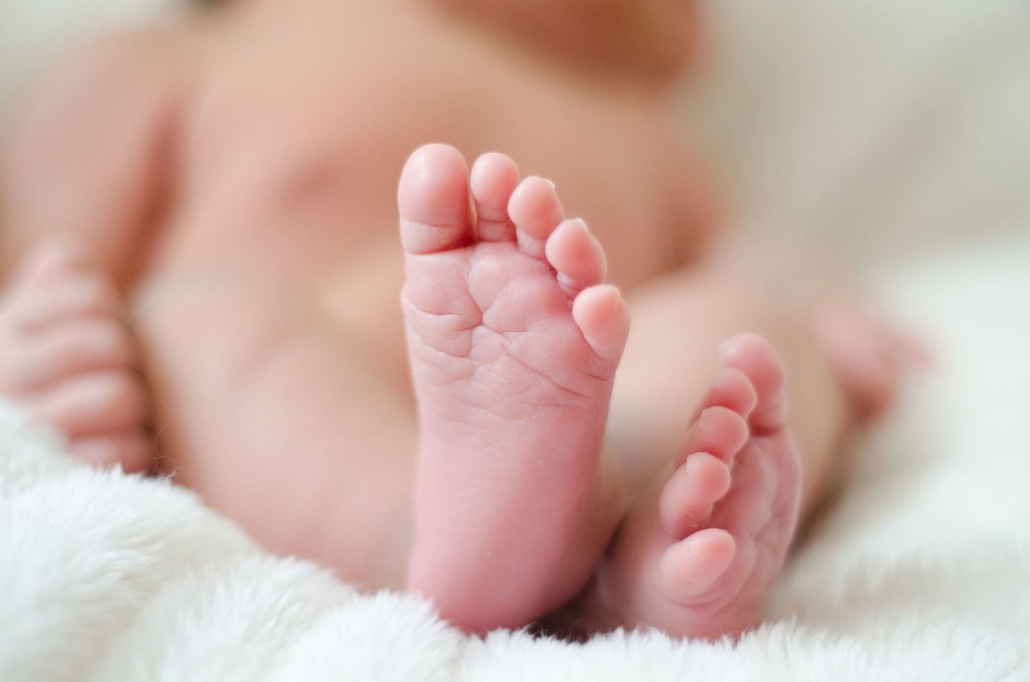 Close-up of tiny baby feet and toes against white fabric.