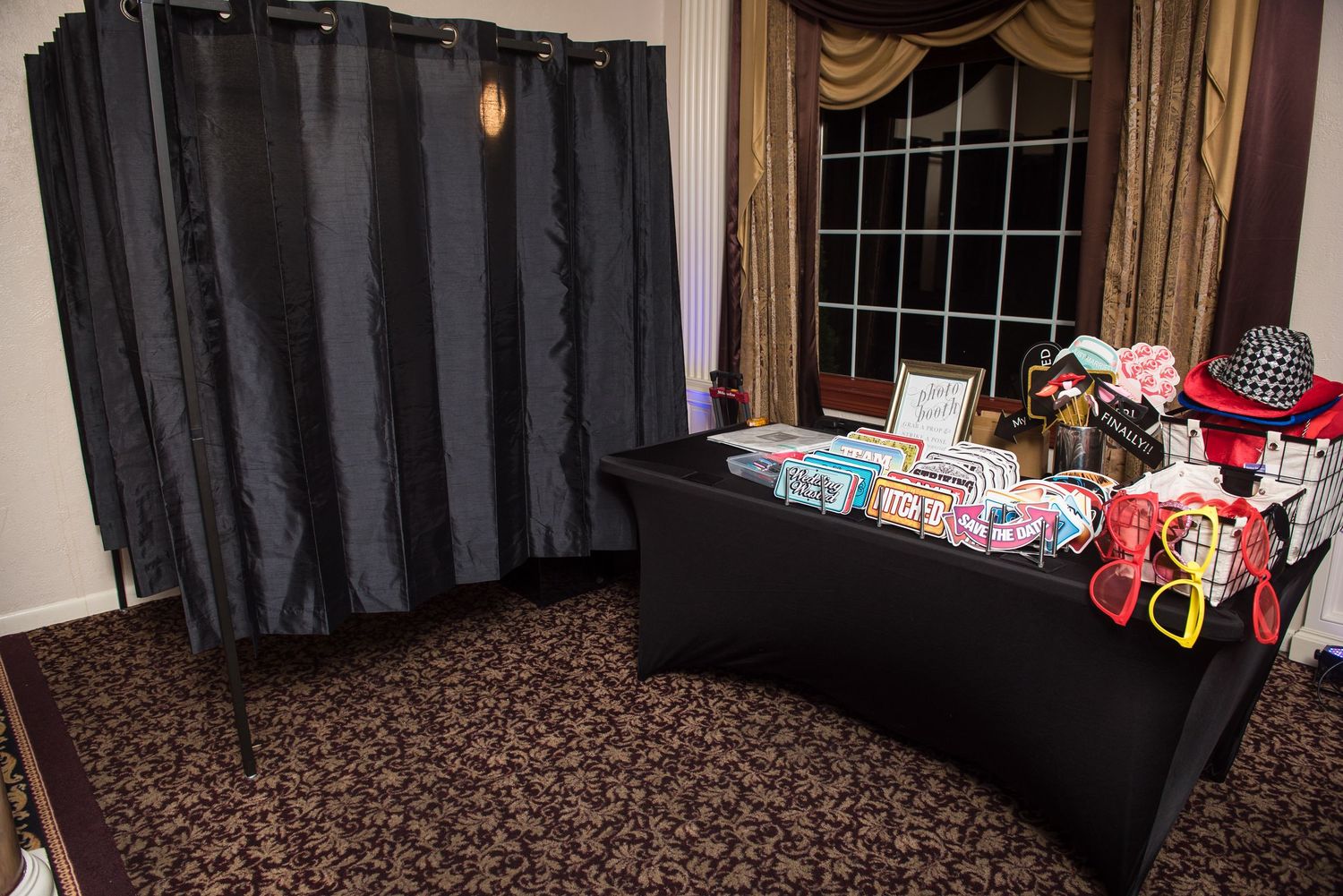 Wedding gift table setup with black tablecloth and backdrop near elegant window treatment.