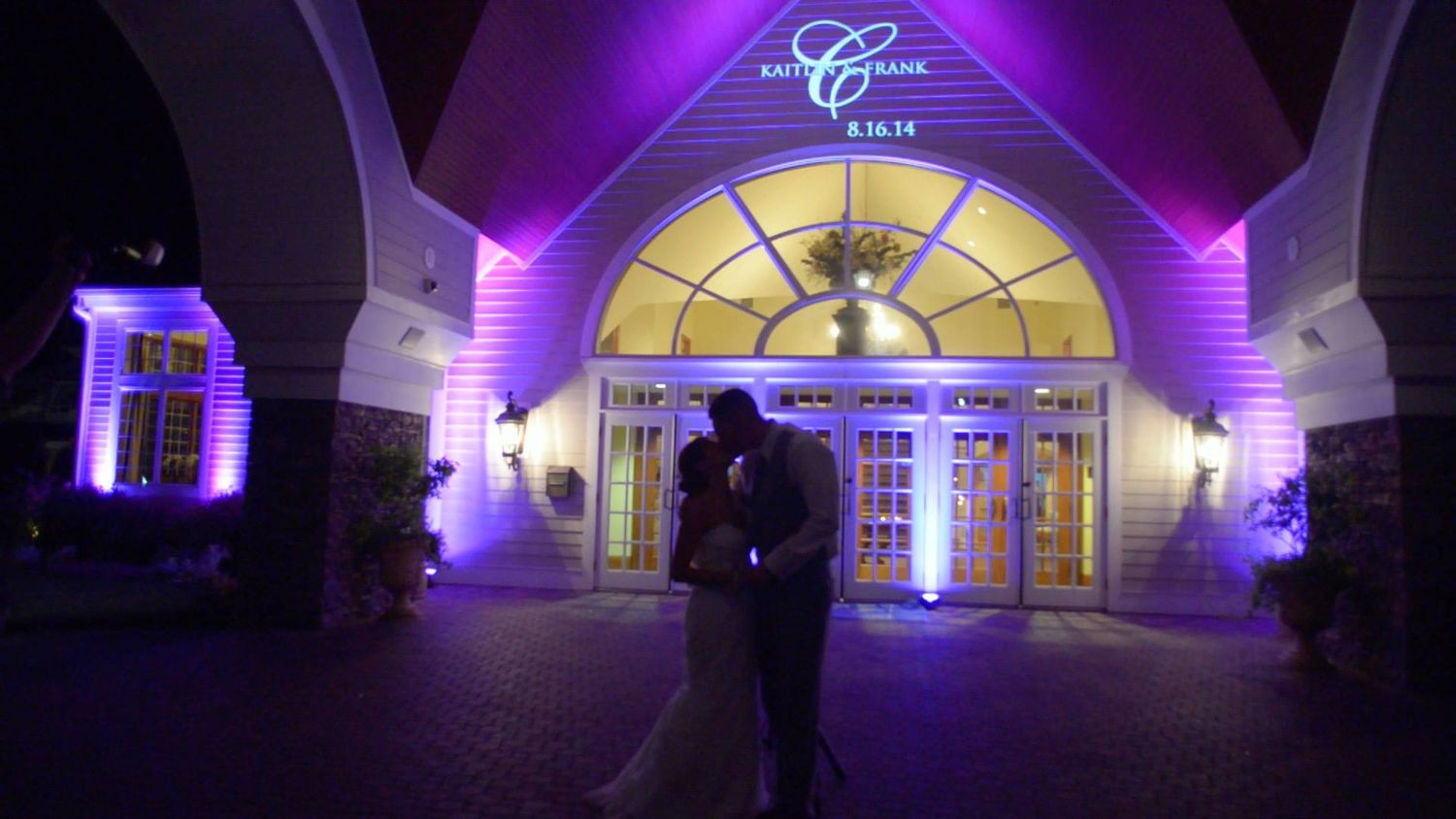 Event venue entrance with arched windows illuminated by purple and yellow lighting.