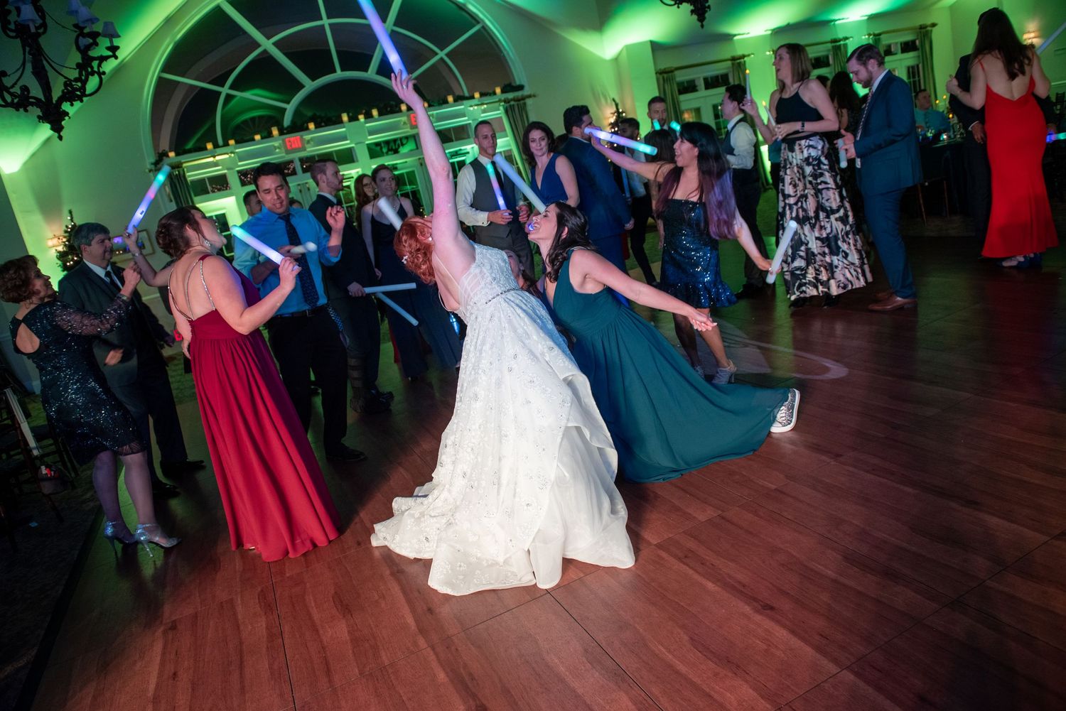 Couples dancing together at a formal event with green lighting and a wooden dance floor.