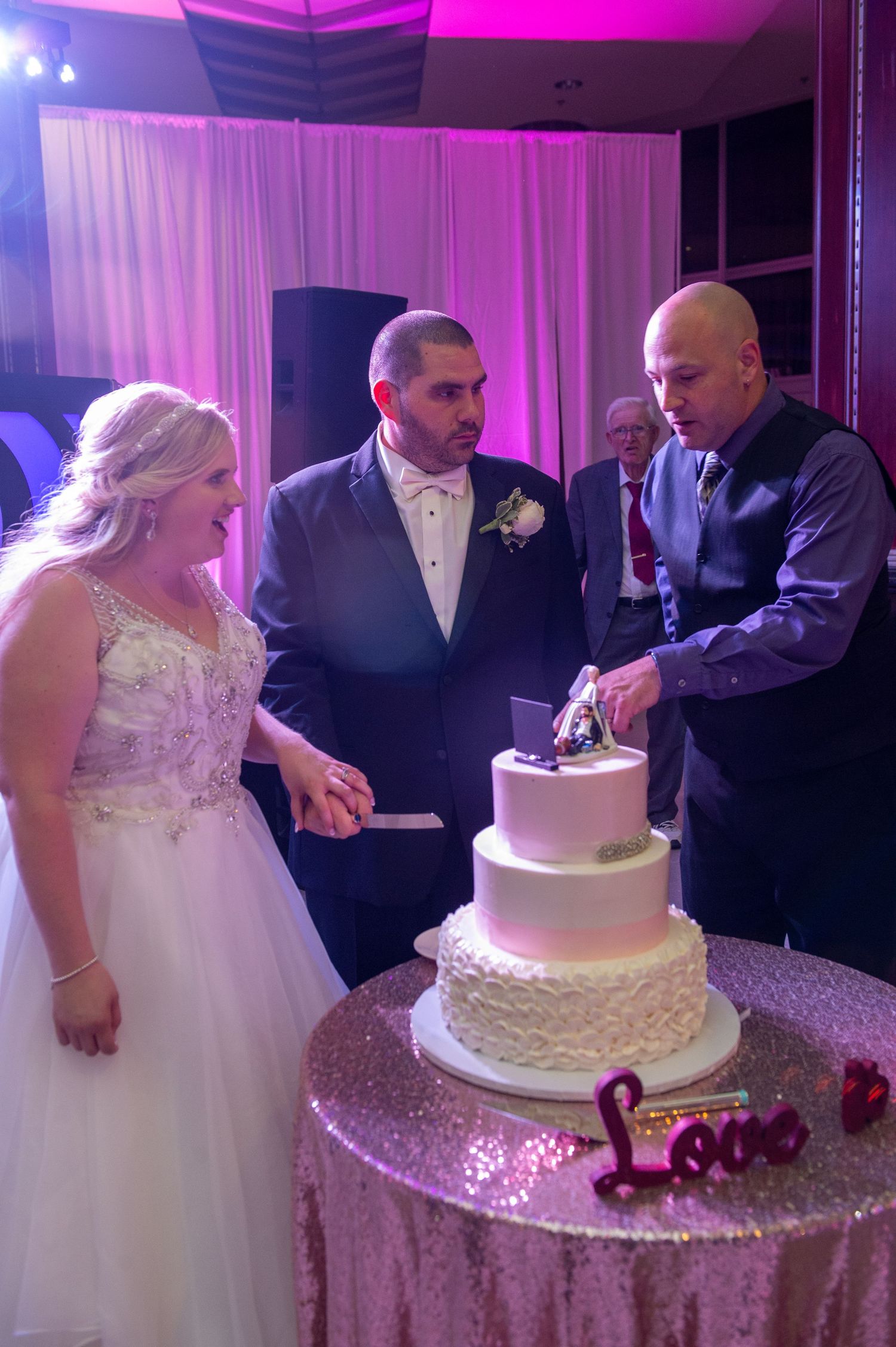 Wedding couple cutting their elegant multi-tiered white cake at reception.