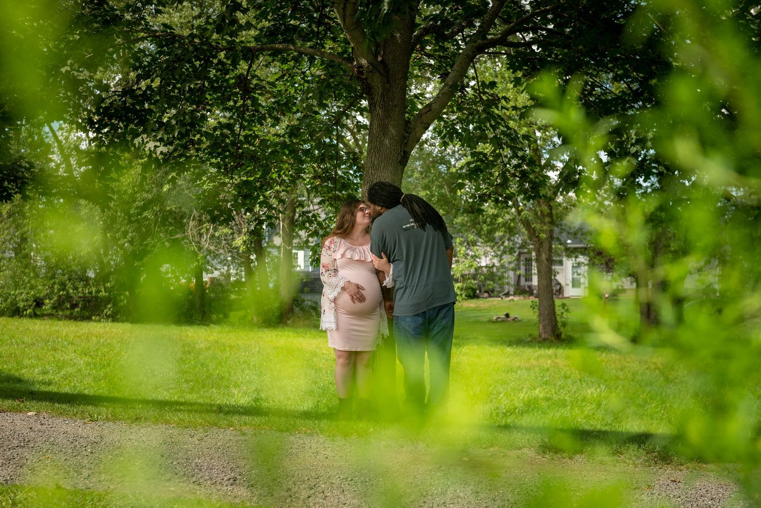 Artistic maternity photos taken through green foliage in a natural outdoor setting.