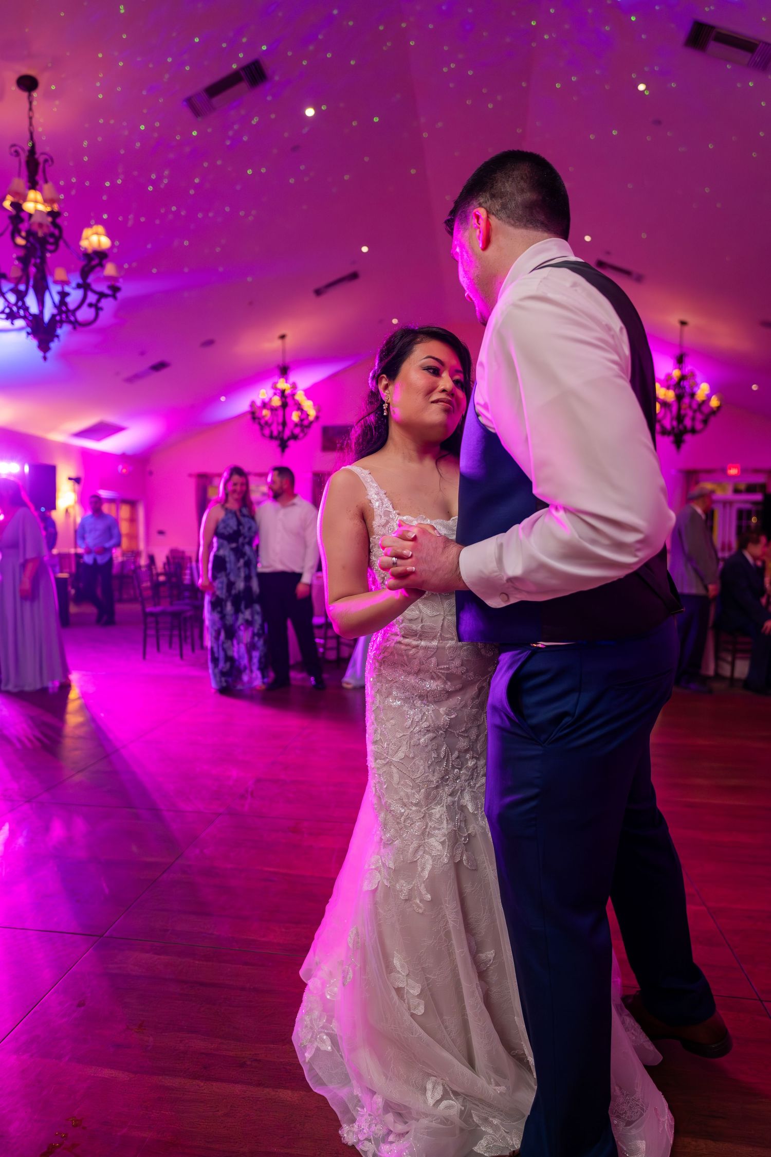 Couple shares intimate dance moment under magenta lighting and sparkly ceiling effects.