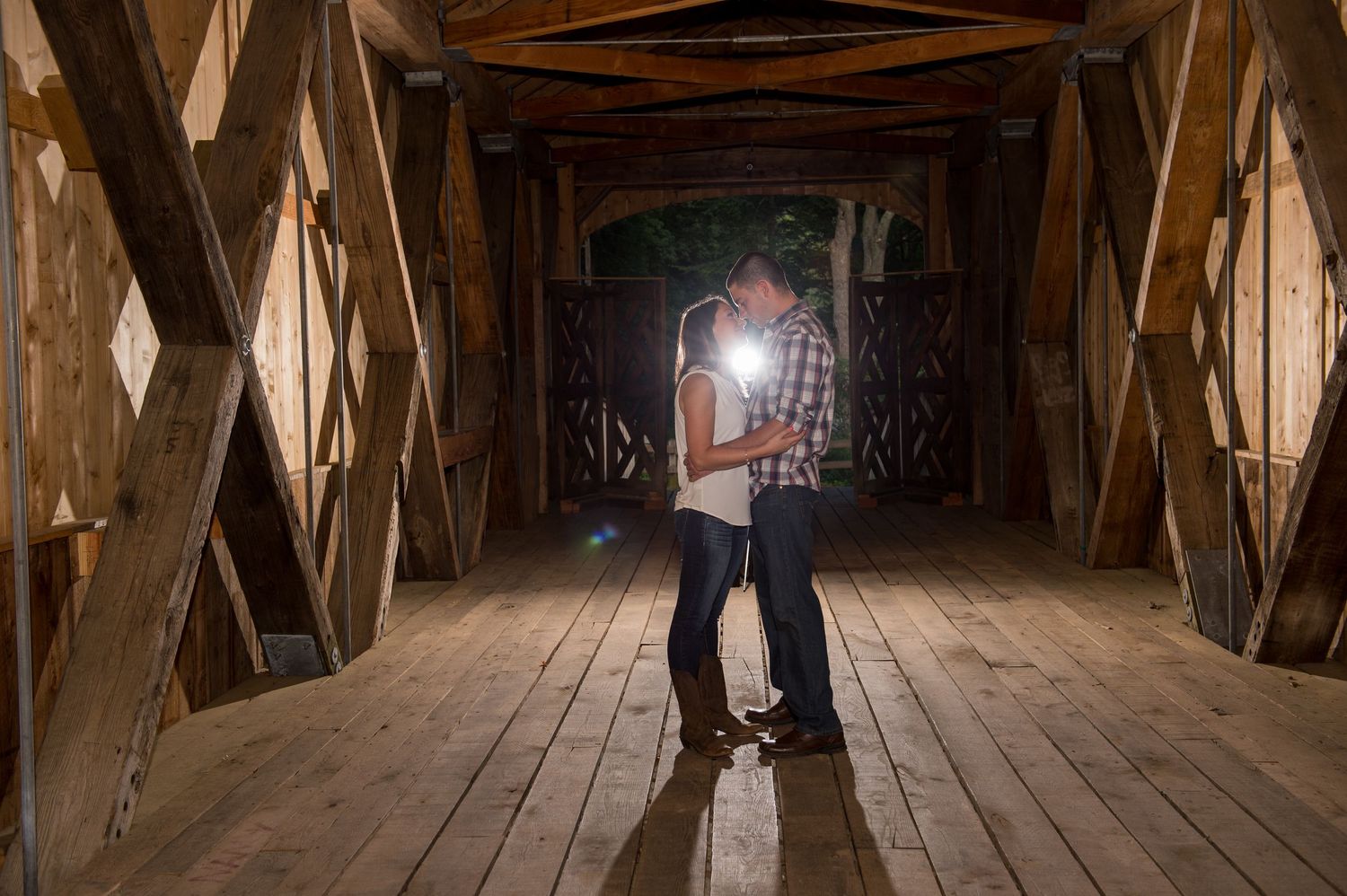 A couple sharing an intimate moment inside a rustic wooden covered bridge.