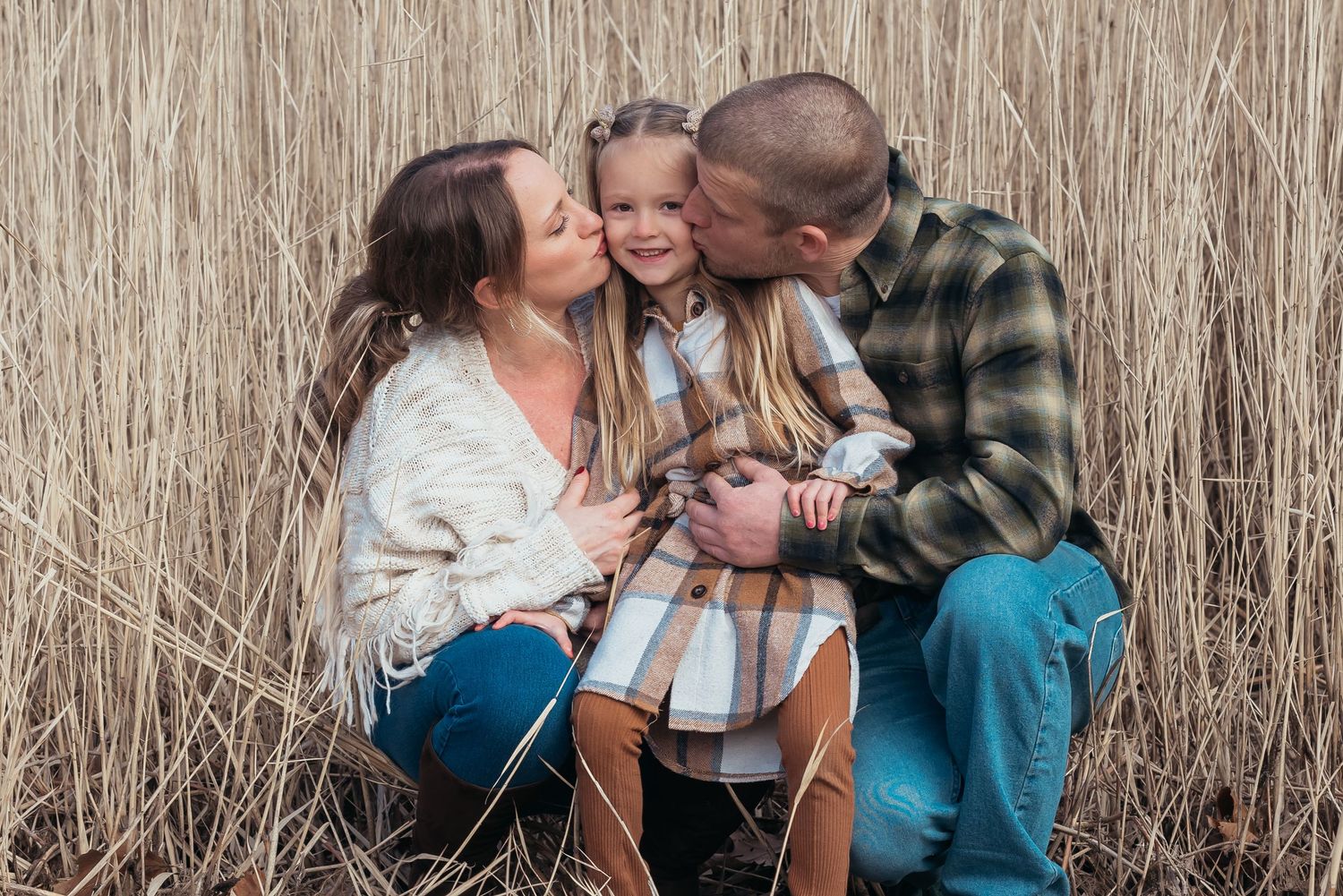 A tender family moment captured among tall dried reeds in a natural setting.
