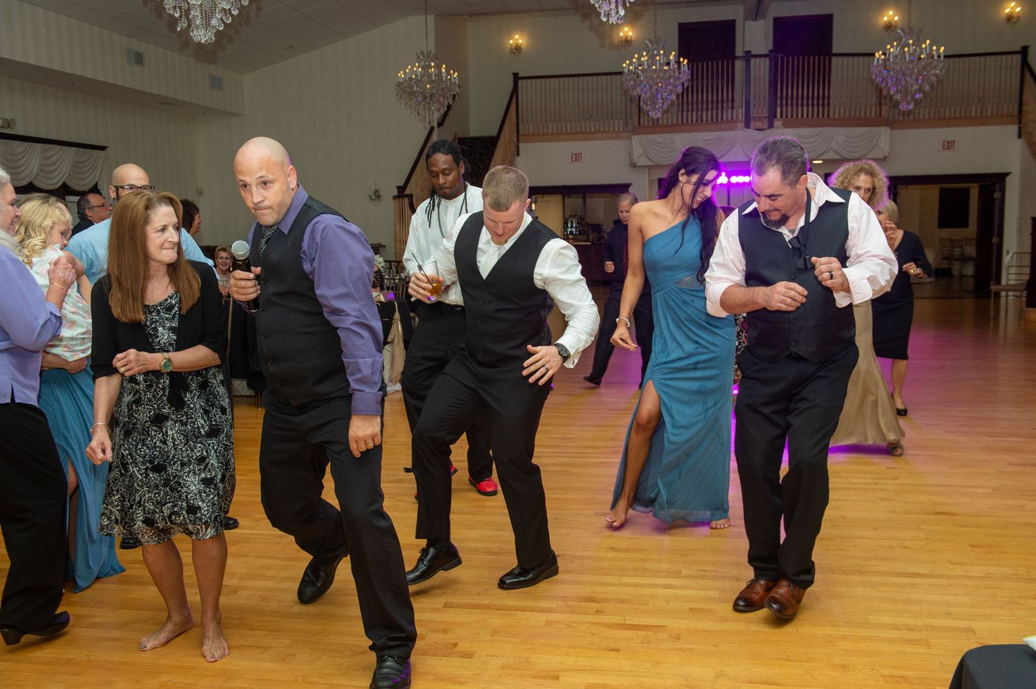 Wedding reception venue with hardwood floors and guests mingling under warm lighting.