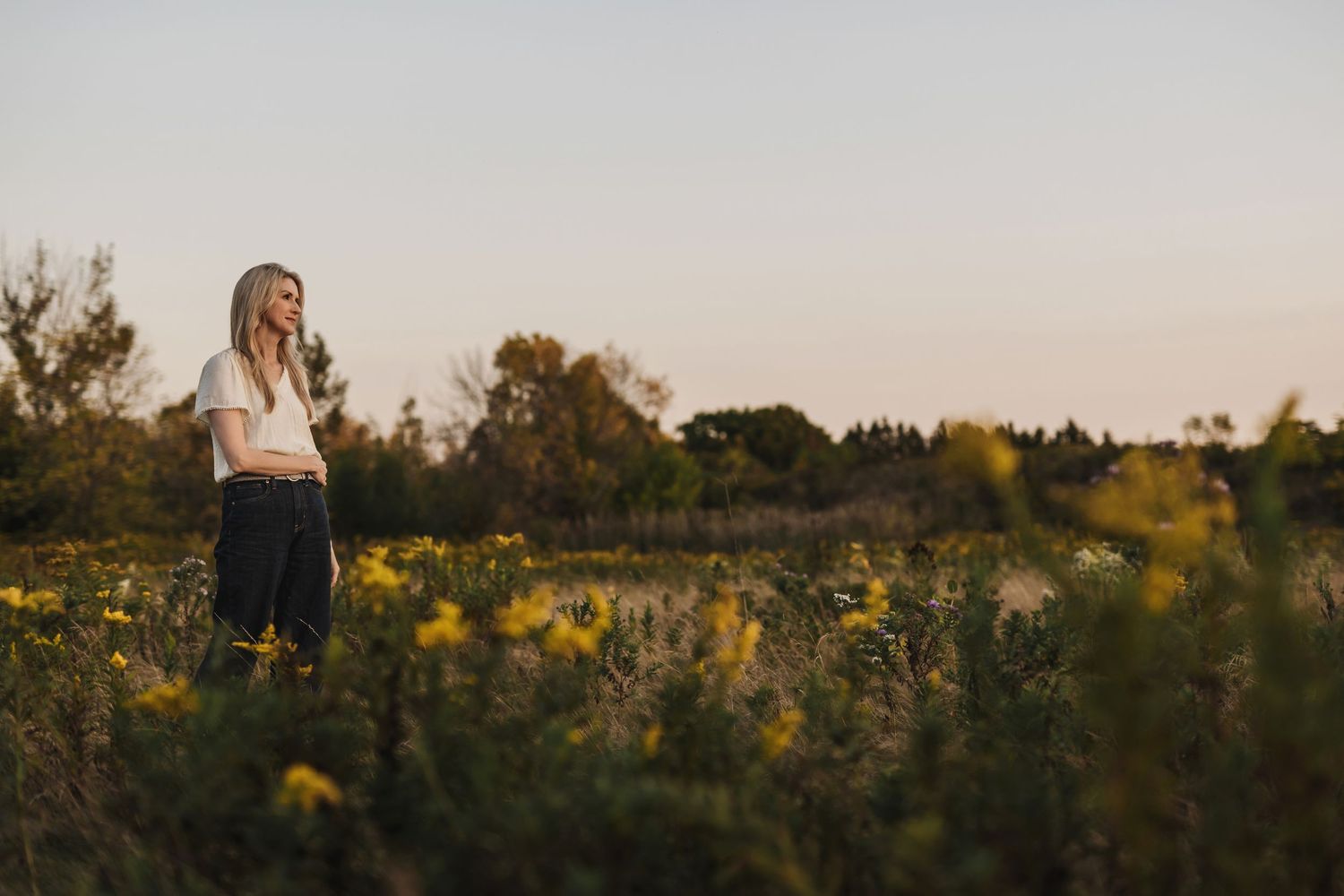 Michelle standing in sunlit meadow with tall grasses and wildflowers at golden hour