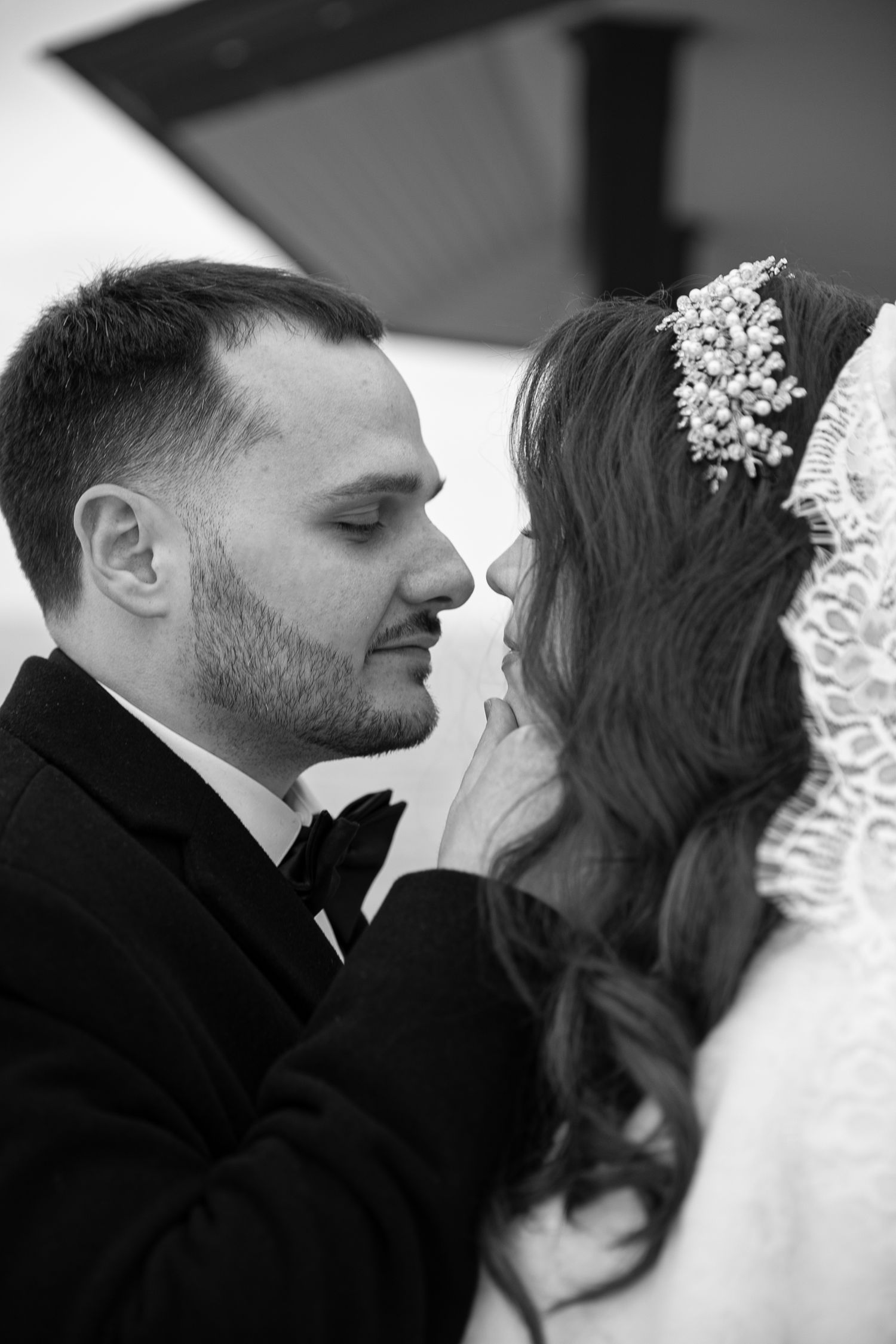 Black and white wedding photo of bride and groom in an intimate moment, bride wearing lace veil with pearl headpiece.