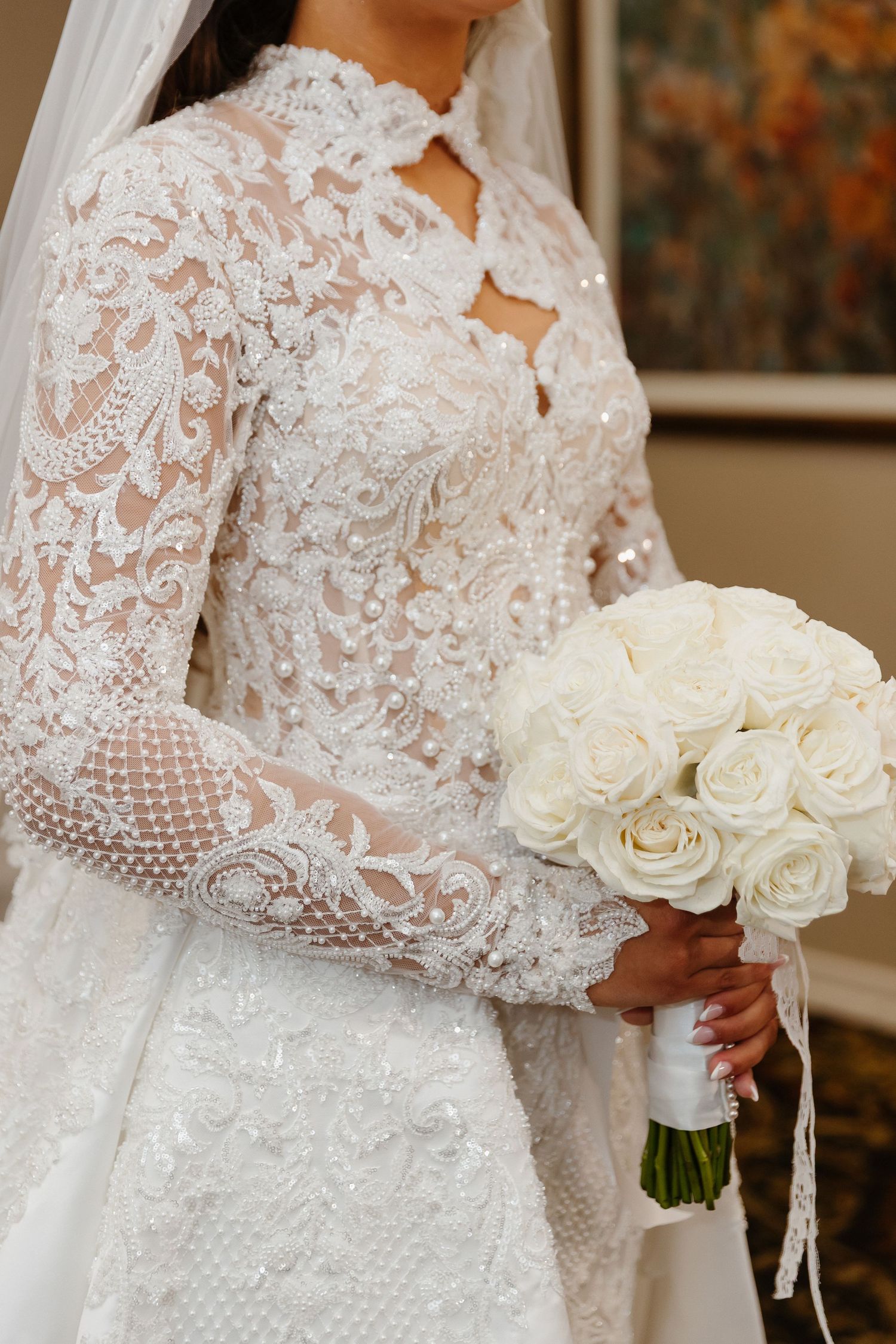 Bride in elegant long-sleeve lace wedding gown holding a bouquet of white roses.