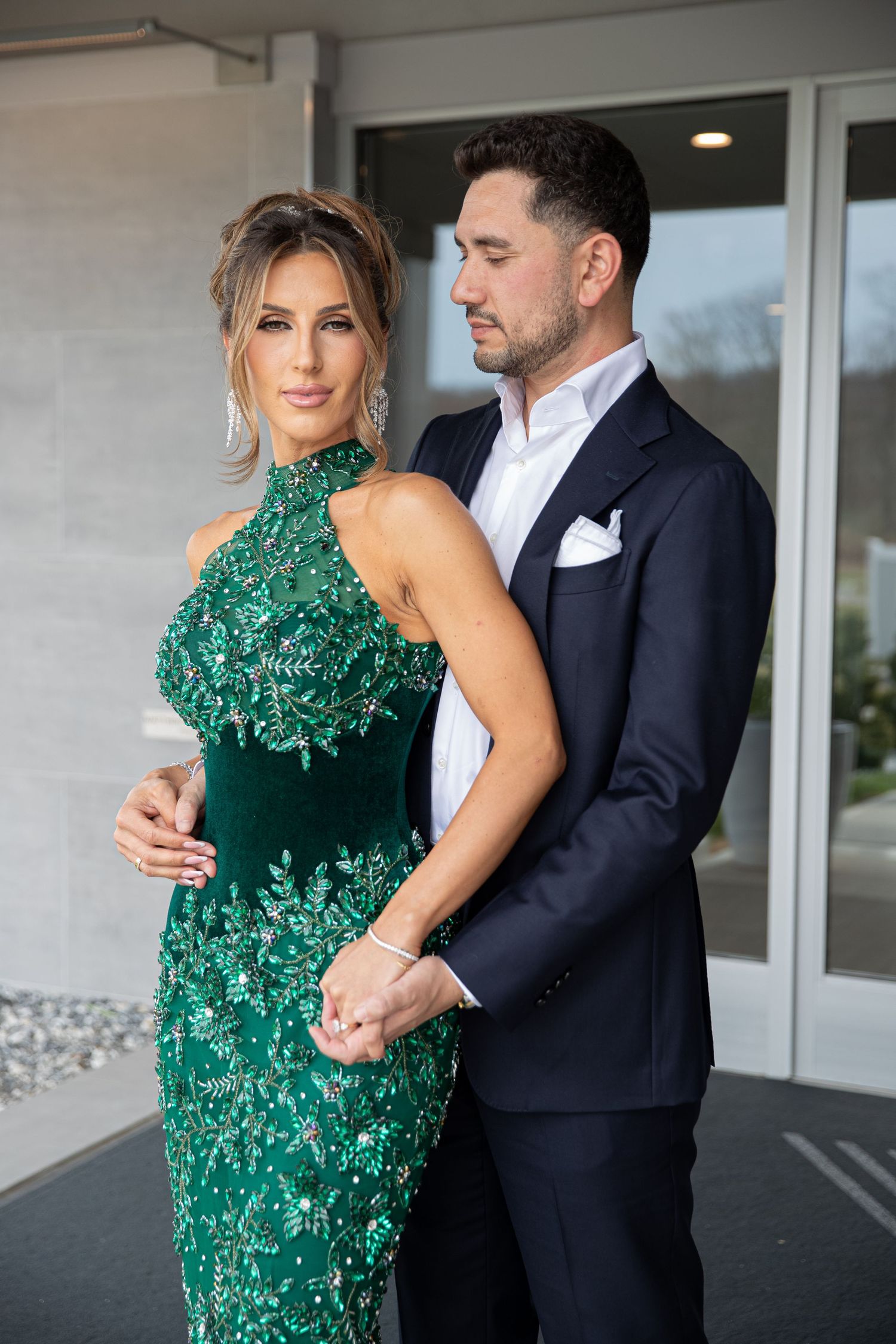 Couple posing elegantly, woman in green beaded gown and man in dark suit with white pocket square.