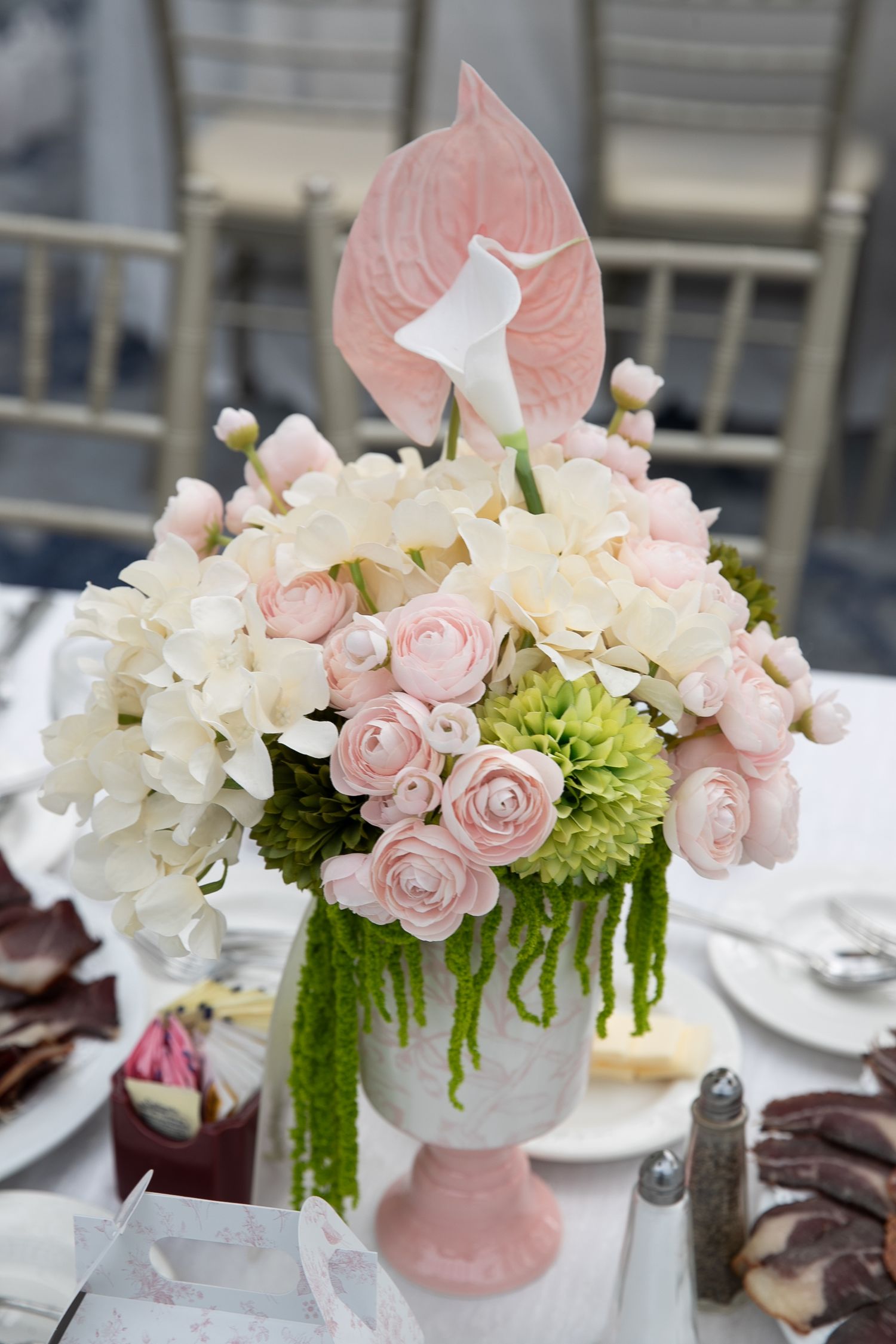 Elegant floral centerpiece with pink roses, white hydrangeas and green amaranthus in a pink and white vase on dining table.