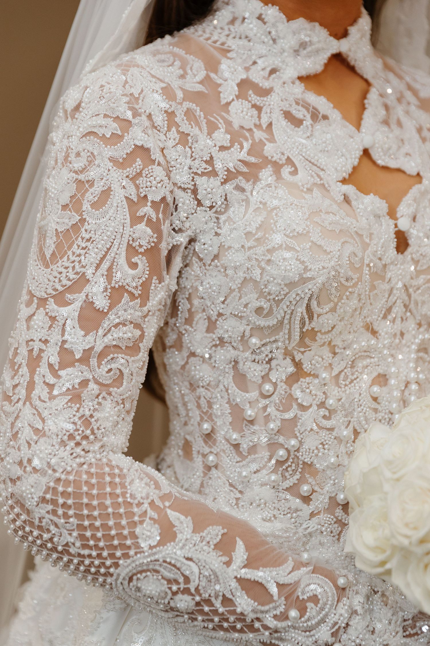 Close-up of a bride wearing an elegant long-sleeve lace wedding gown adorned with intricate beading and pearl embellishments.