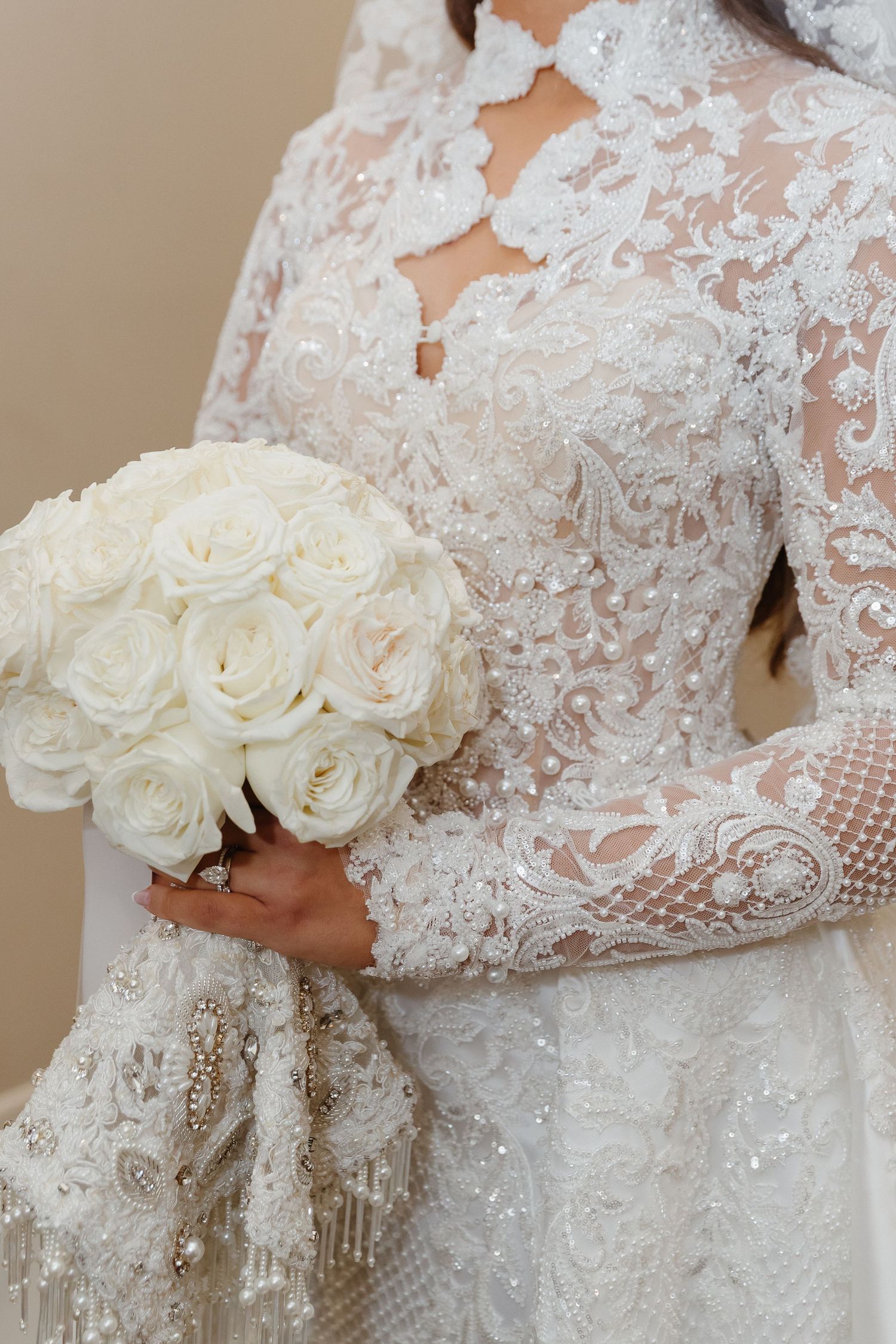 Bride in elegant white lace long-sleeve wedding gown holding a bouquet of white roses with pearl and beaded details.