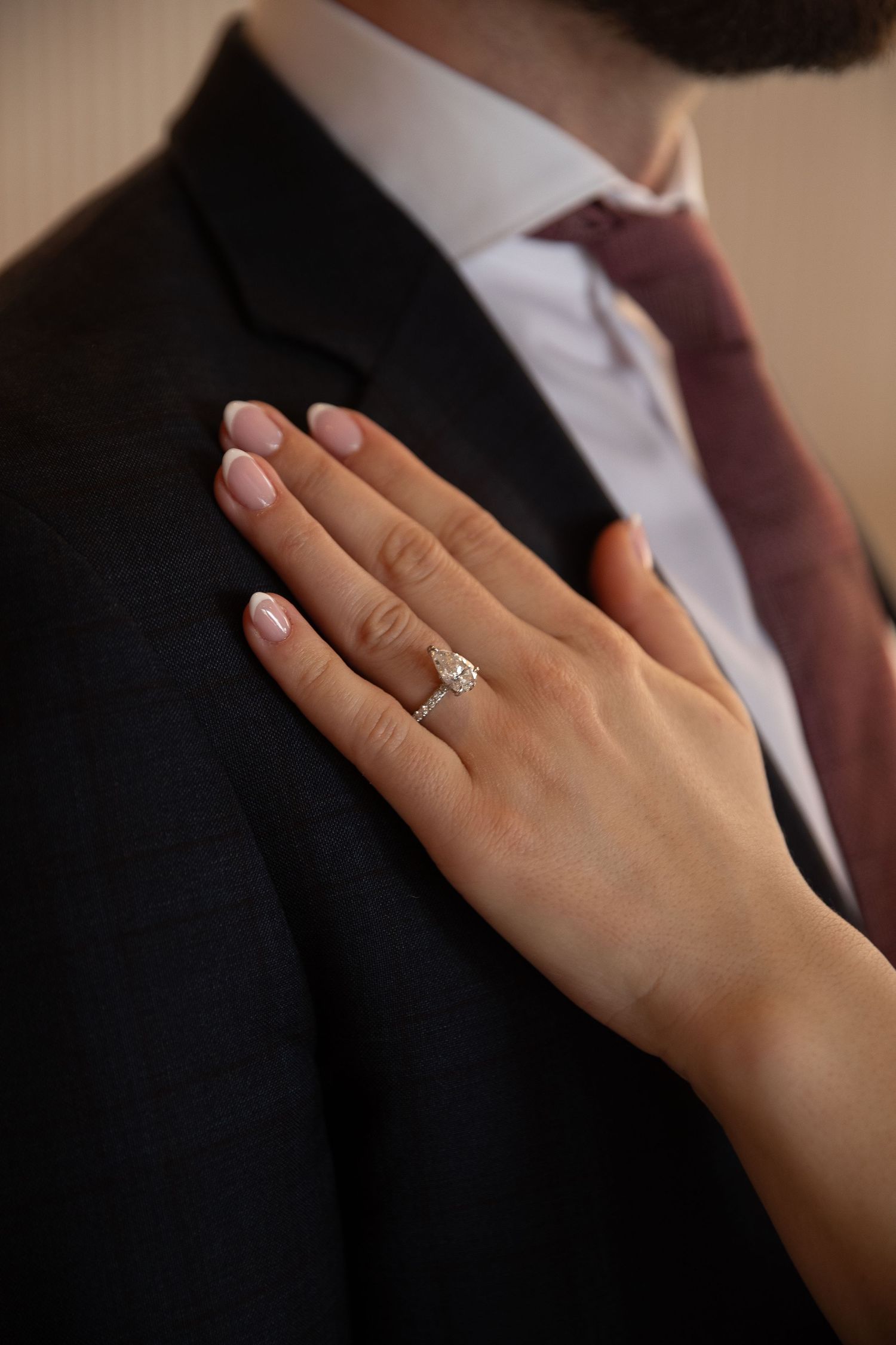 A woman's hand with a diamond engagement ring resting on a man's dark suit jacket.