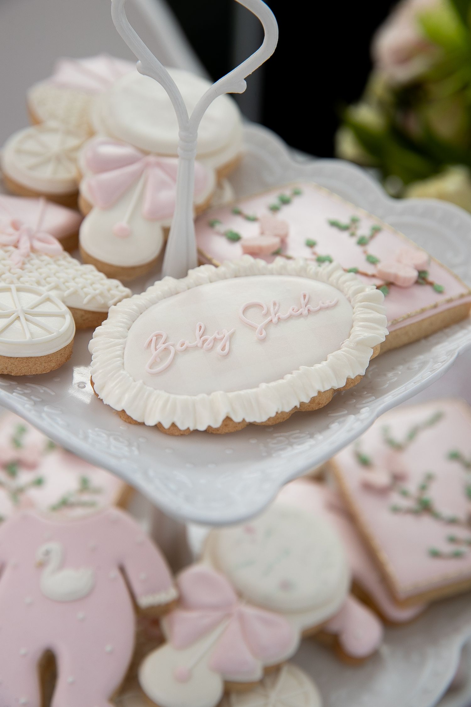 Pink and white baby shower cookies with swan, carriage, and Baby Shower inscription on a tiered display stand.