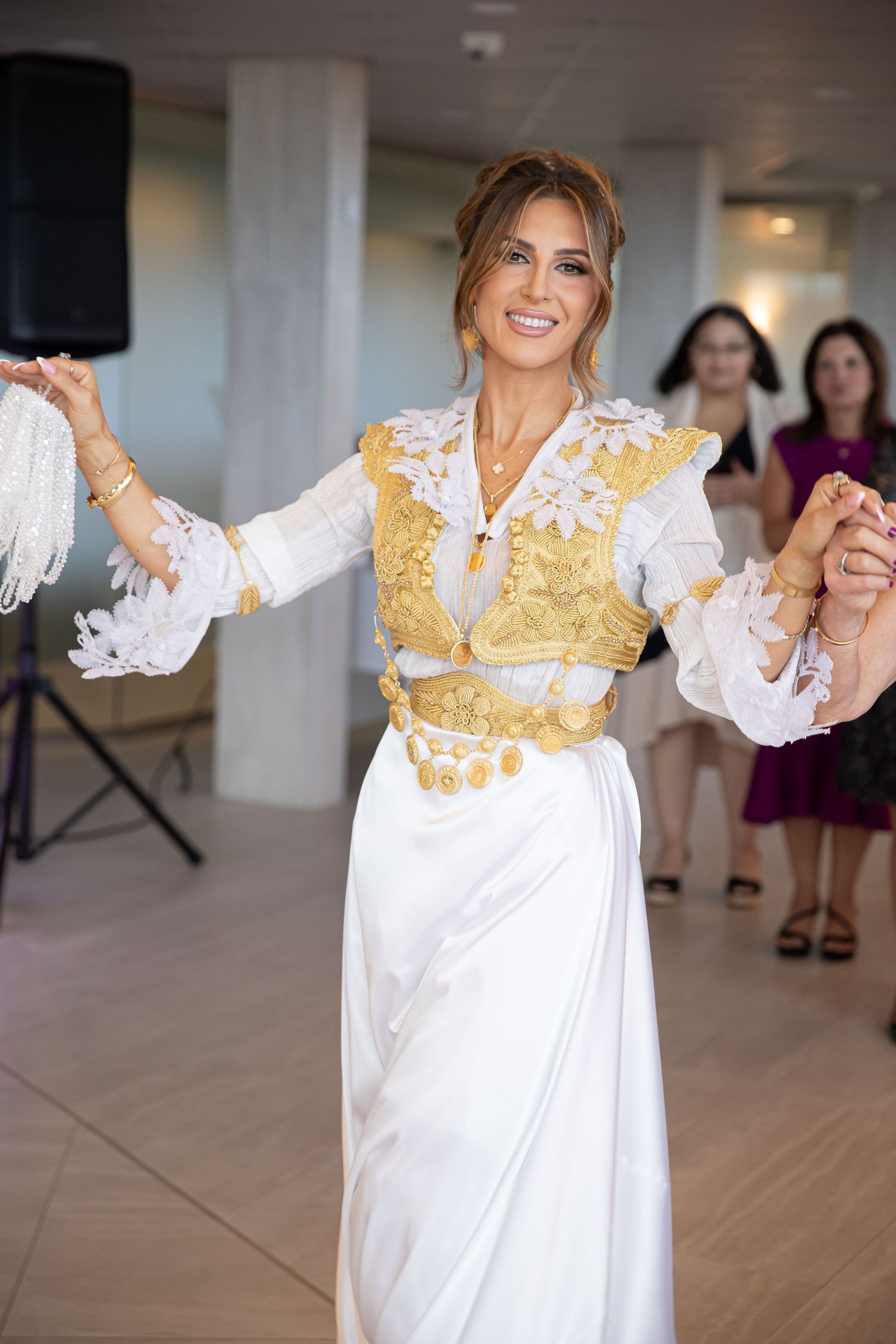 Woman in traditional white and gold embroidered costume dancing gracefully at a celebration event.