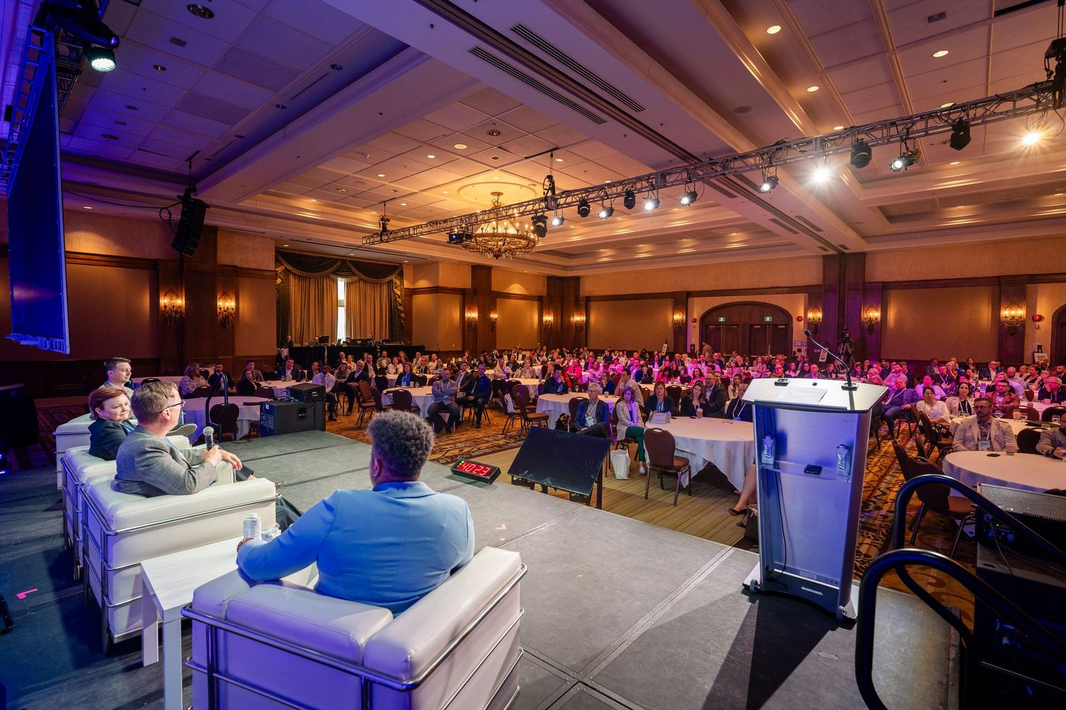 Wide angle view of conference hall with audience and stage lighting.