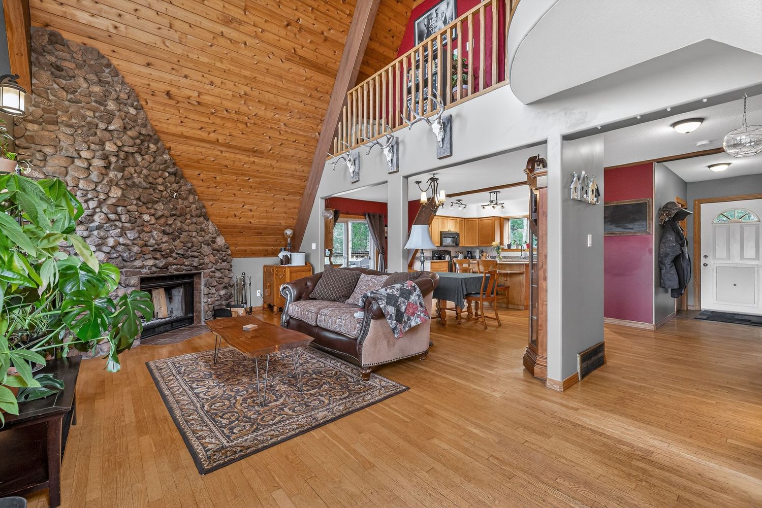 Rustic living room featuring a stone fireplace, wood-paneled vaulted ceiling, hardwood floors, and open layout.
