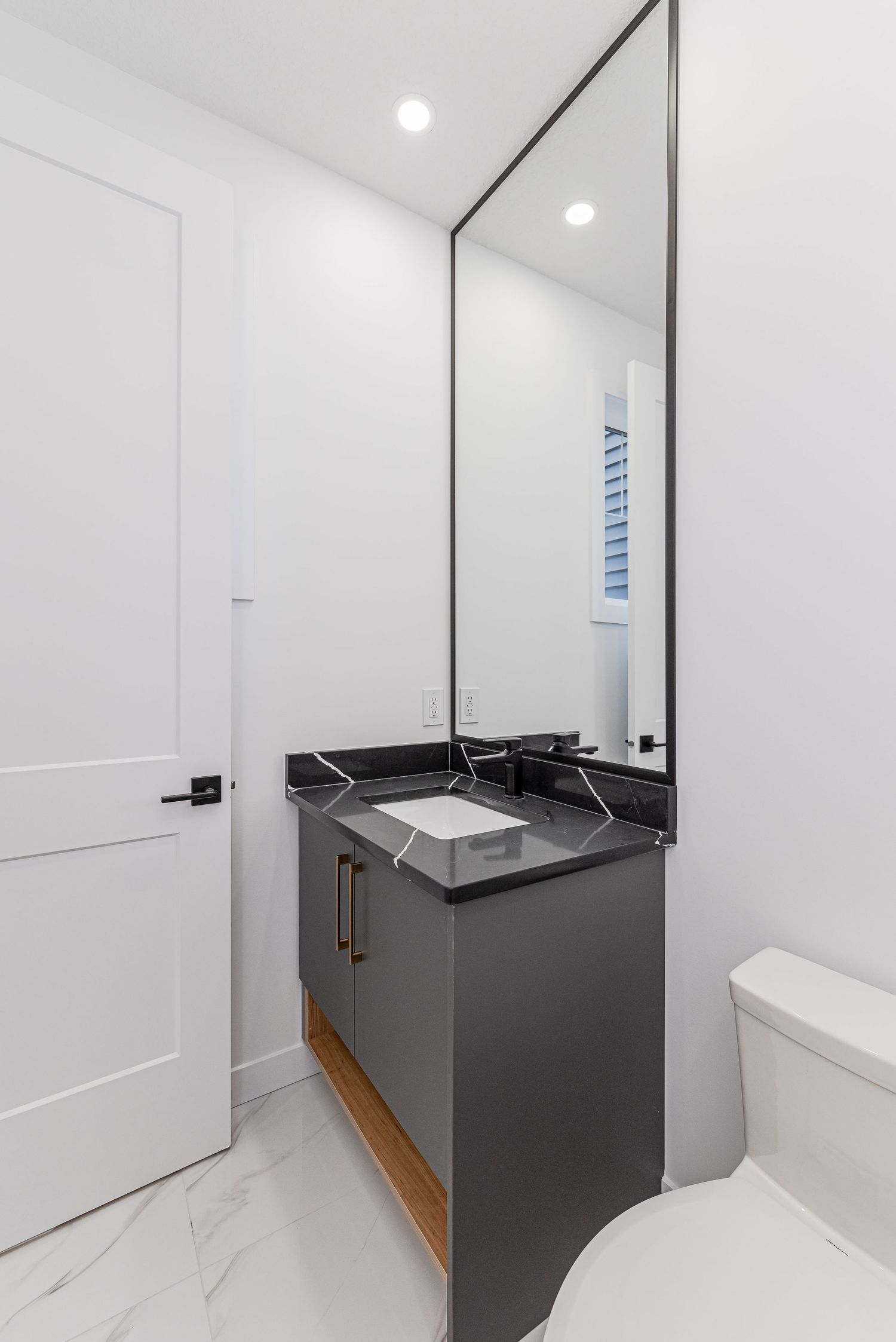 Modern bathroom with gray vanity, black marble countertop, tall mirror, and white marble floors.