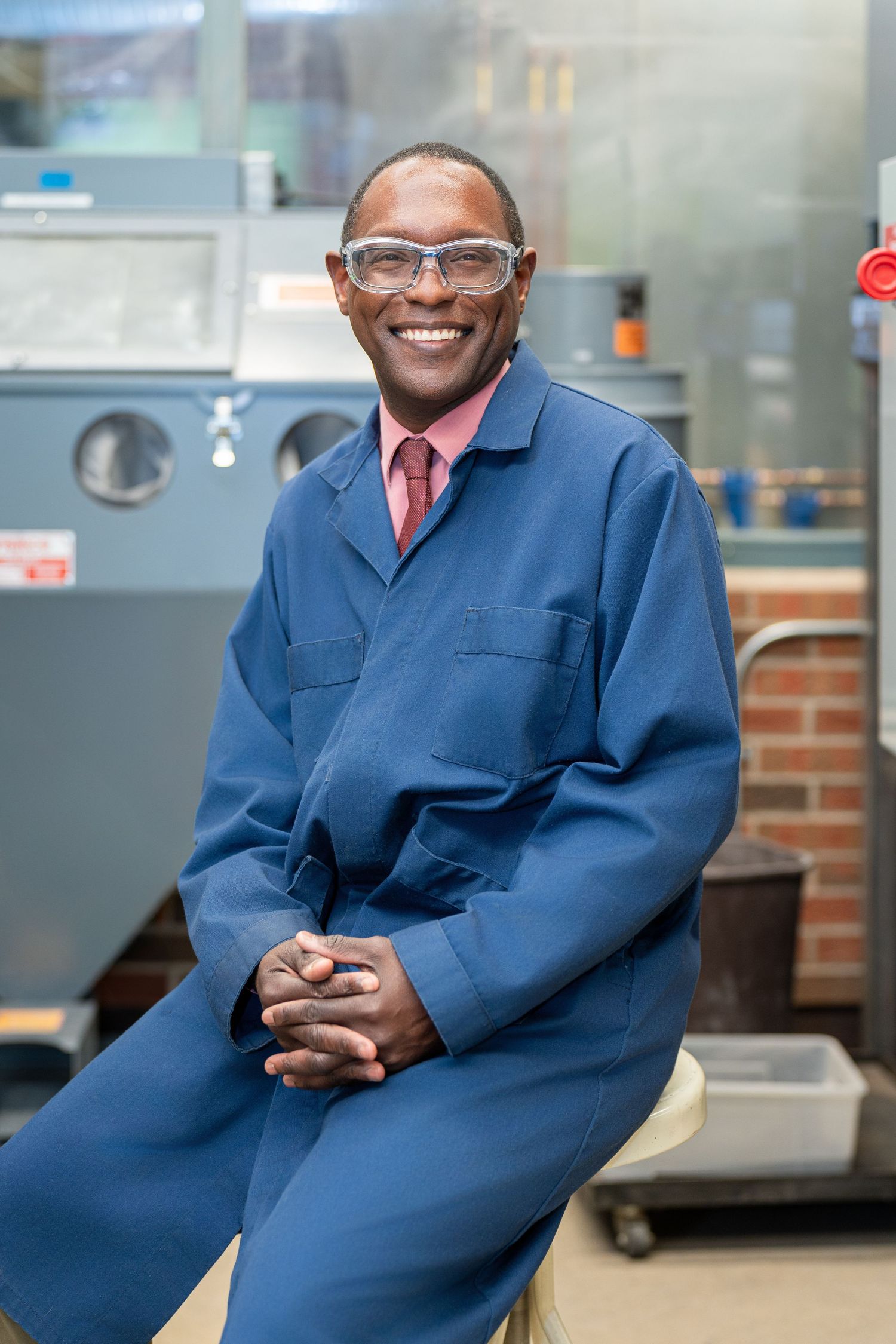 Professional in blue coat seated in laboratory environment with scientific equipment.