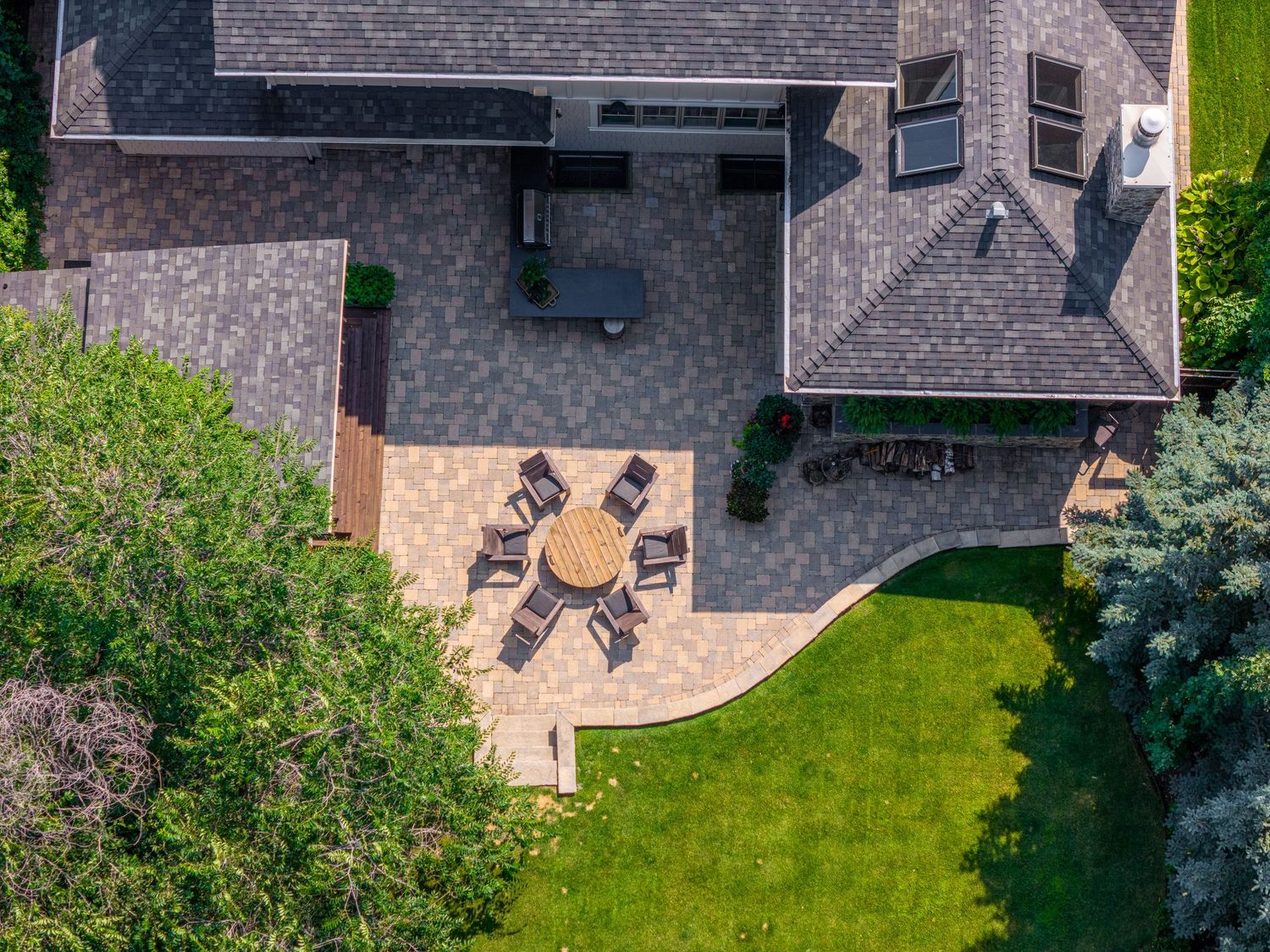 Aerial view of a backyard patio with circular dining set, stone pavers, outdoor seating area, and lush green lawn.