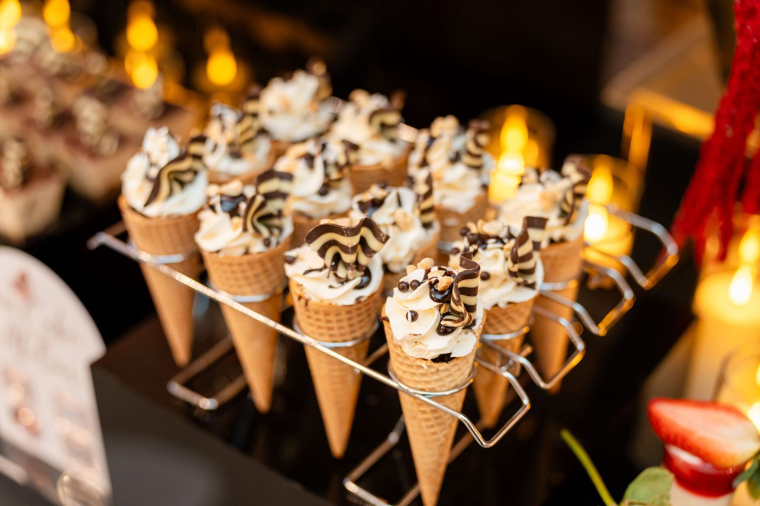 Decorative ice cream cones filled with whipped cream and chocolate drizzle arranged in metal holders.