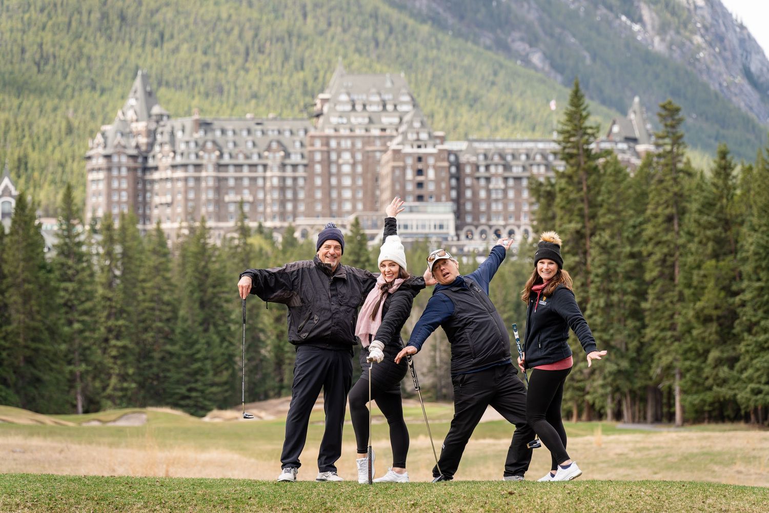 Group poses playfully on grass with the iconic Fairmont Banff Springs Hotel and mountains in the background.