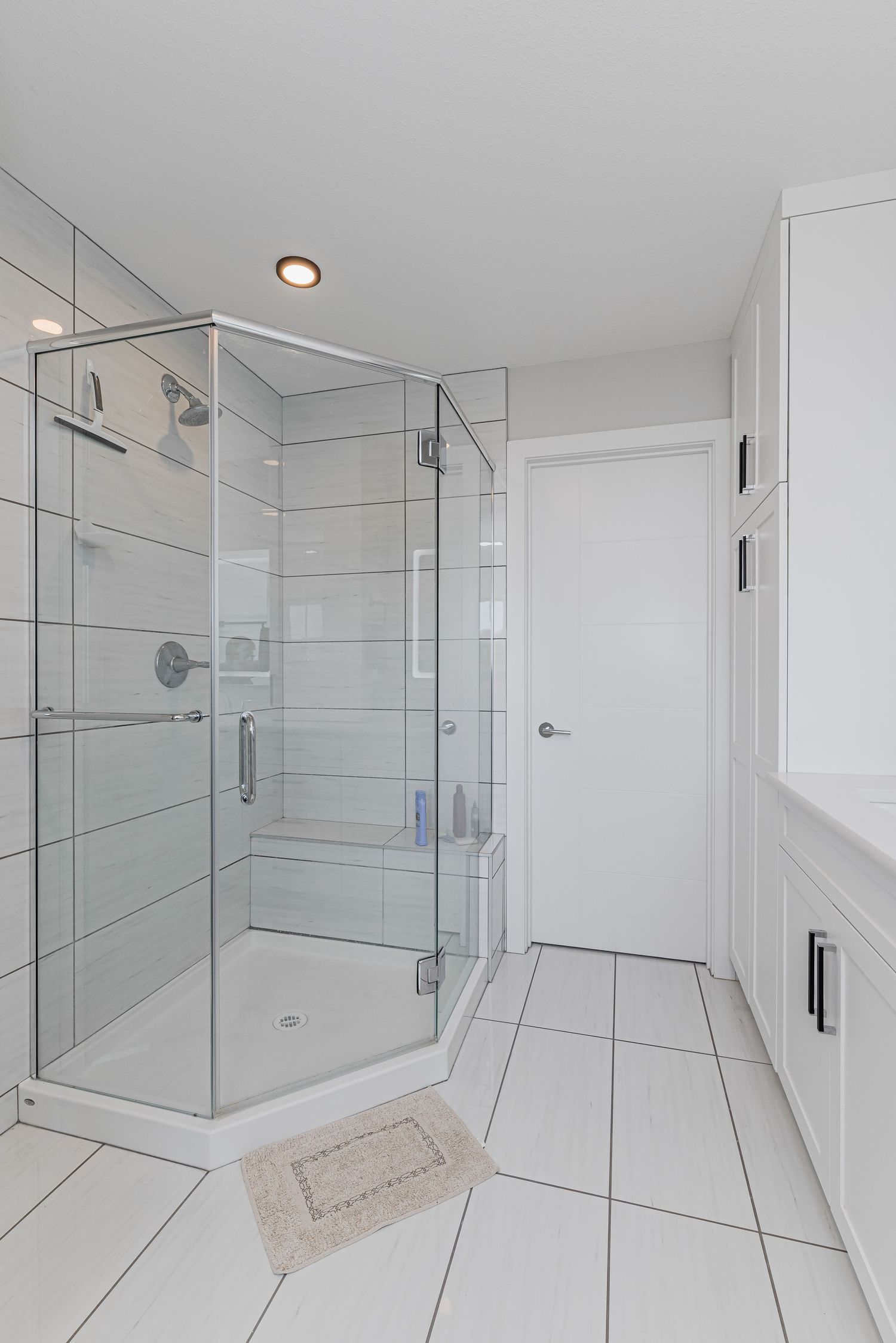 Modern bathroom with glass corner shower enclosure, white tile flooring, and built-in cabinetry.