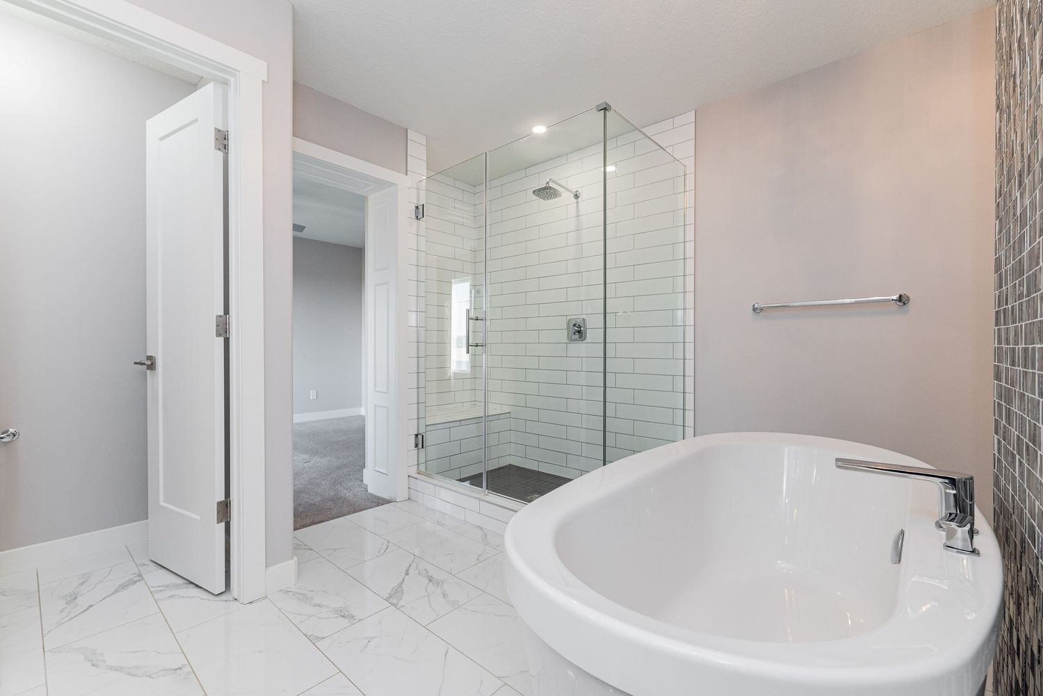 Modern bathroom with freestanding soaking tub, glass walk-in shower, marble tile floors, and open door to bedroom.