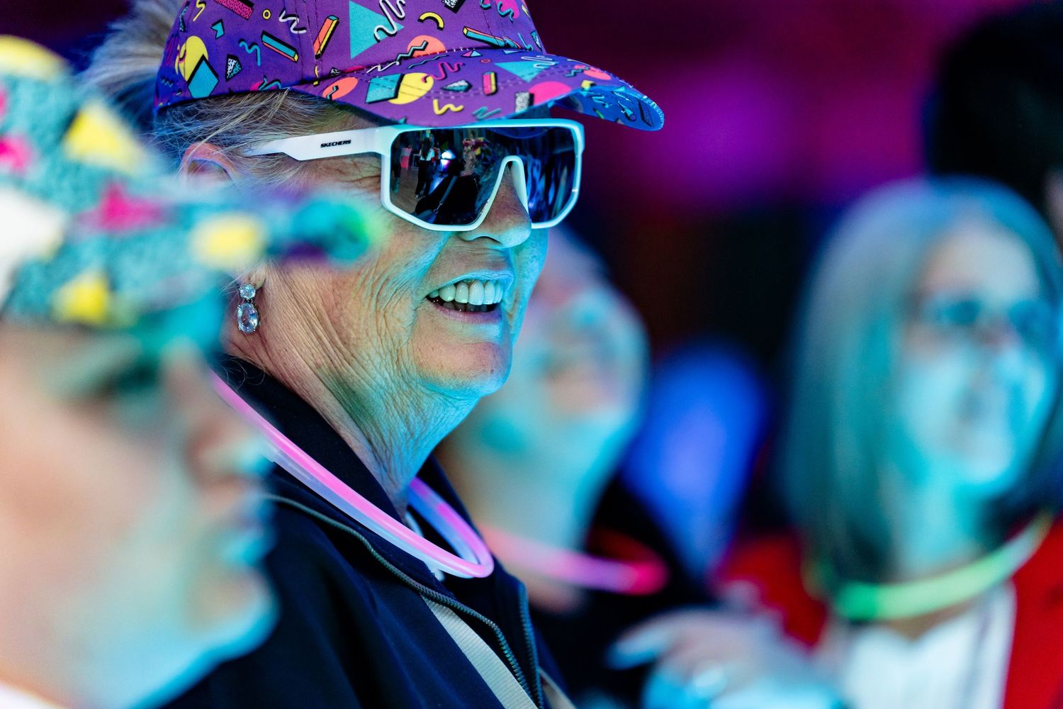 Partygoer wearing colorful hat and sunglasses amid festive purple lighting.