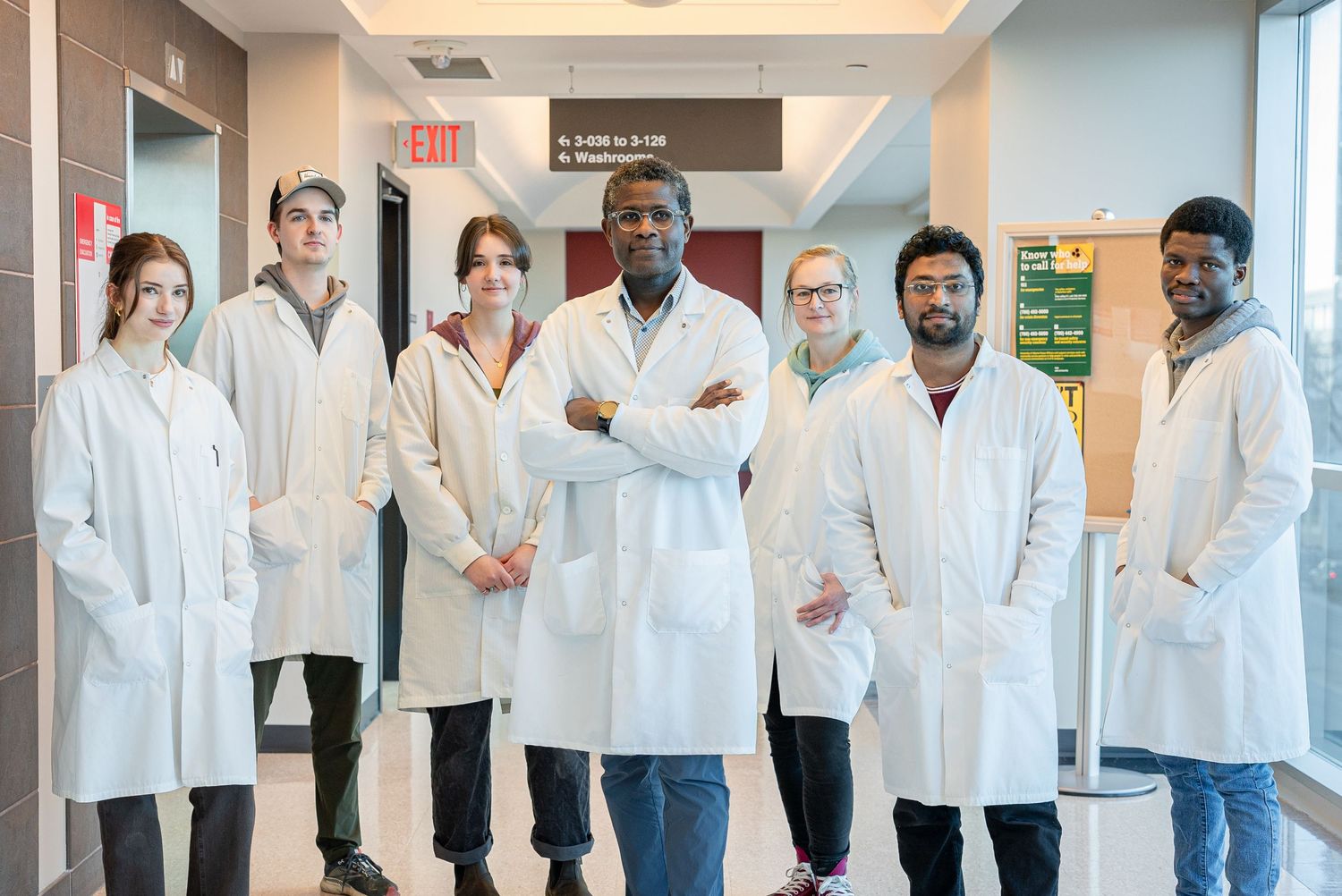 Diverse medical research team poses in hospital hallway wearing white lab coats.