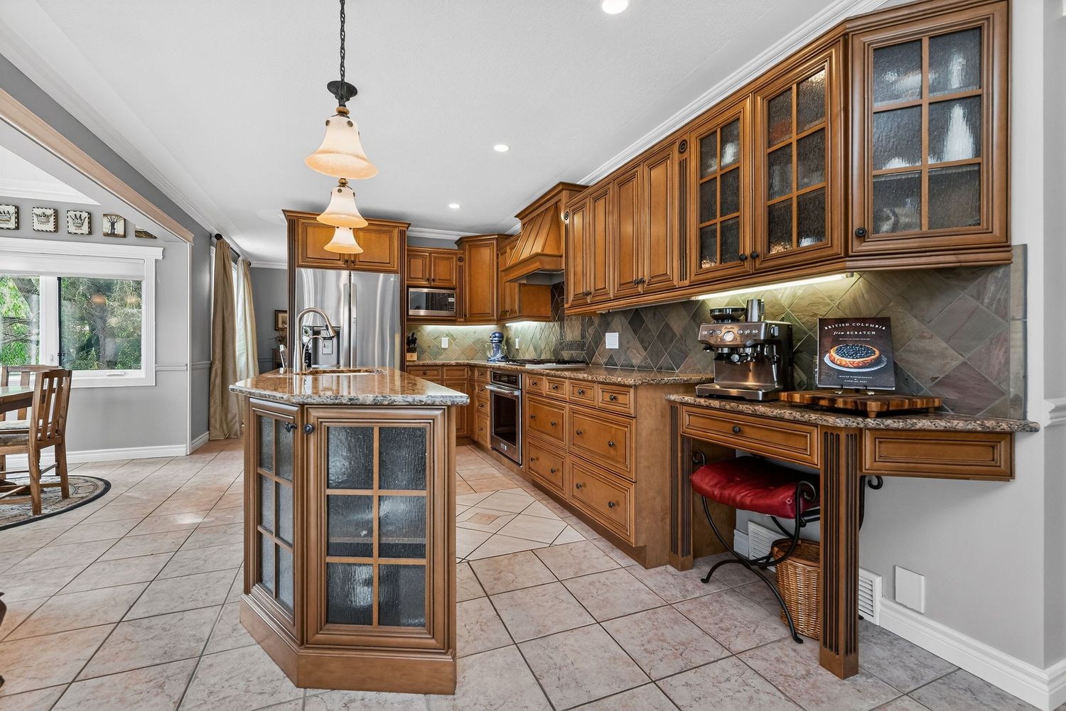 Elegant kitchen with wood cabinetry, granite countertops, tile backsplash, center island, and stainless steel appliances.
