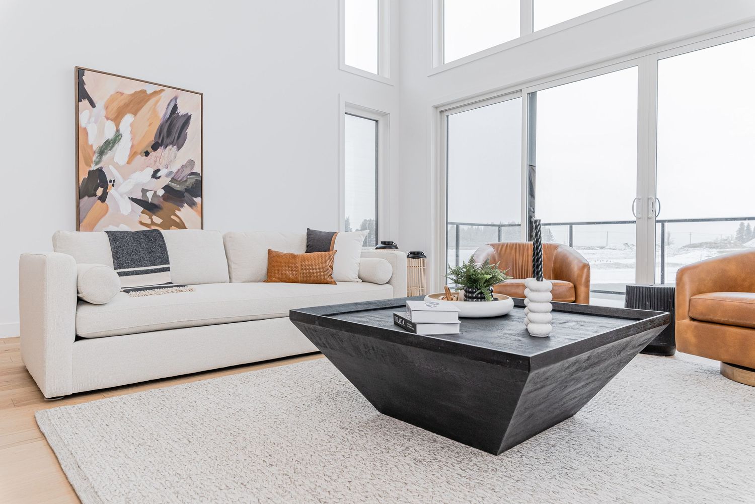 Modern living room with white sofa, black geometric coffee table, and large windows offering natural light.