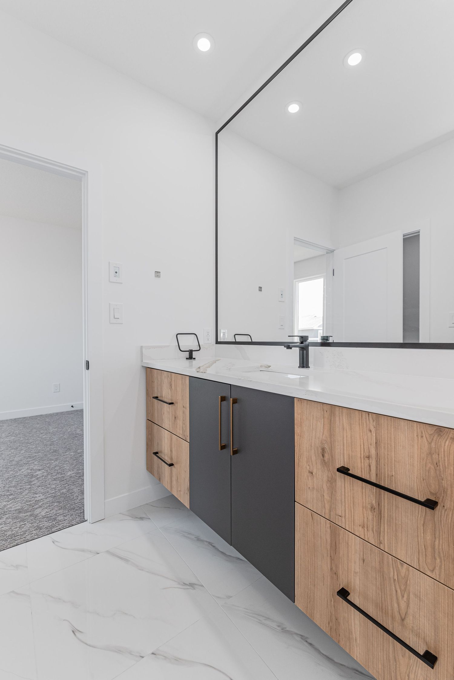 Modern floating bathroom vanity with wood and dark gray drawers, marble floors, black hardware, and large mirror.
