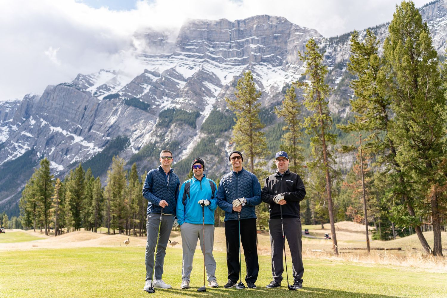 Group gathering at a golf course with dramatic Rocky Mountain peaks in the background.
