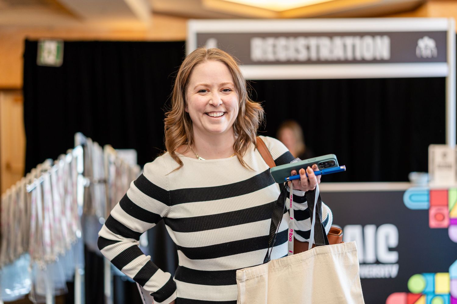 Conference attendee in striped sweater smiles while shopping at registration area.