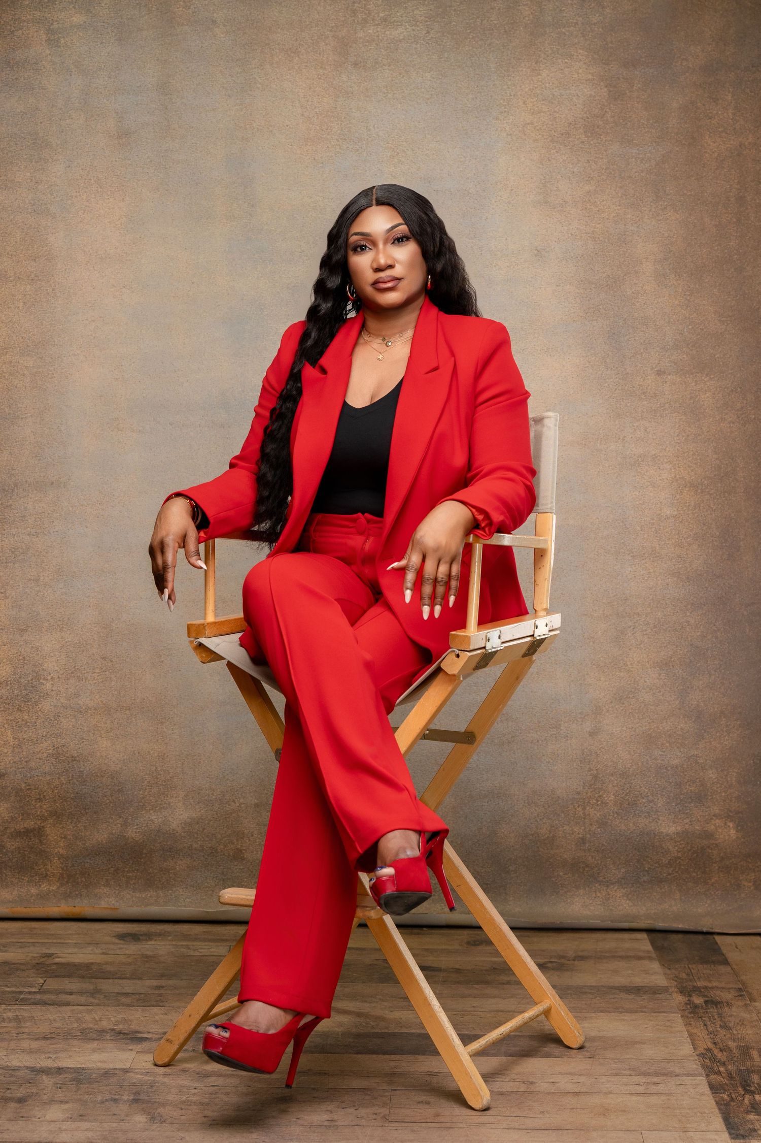 Professional portrait session in red pantsuit on wooden director's chair.