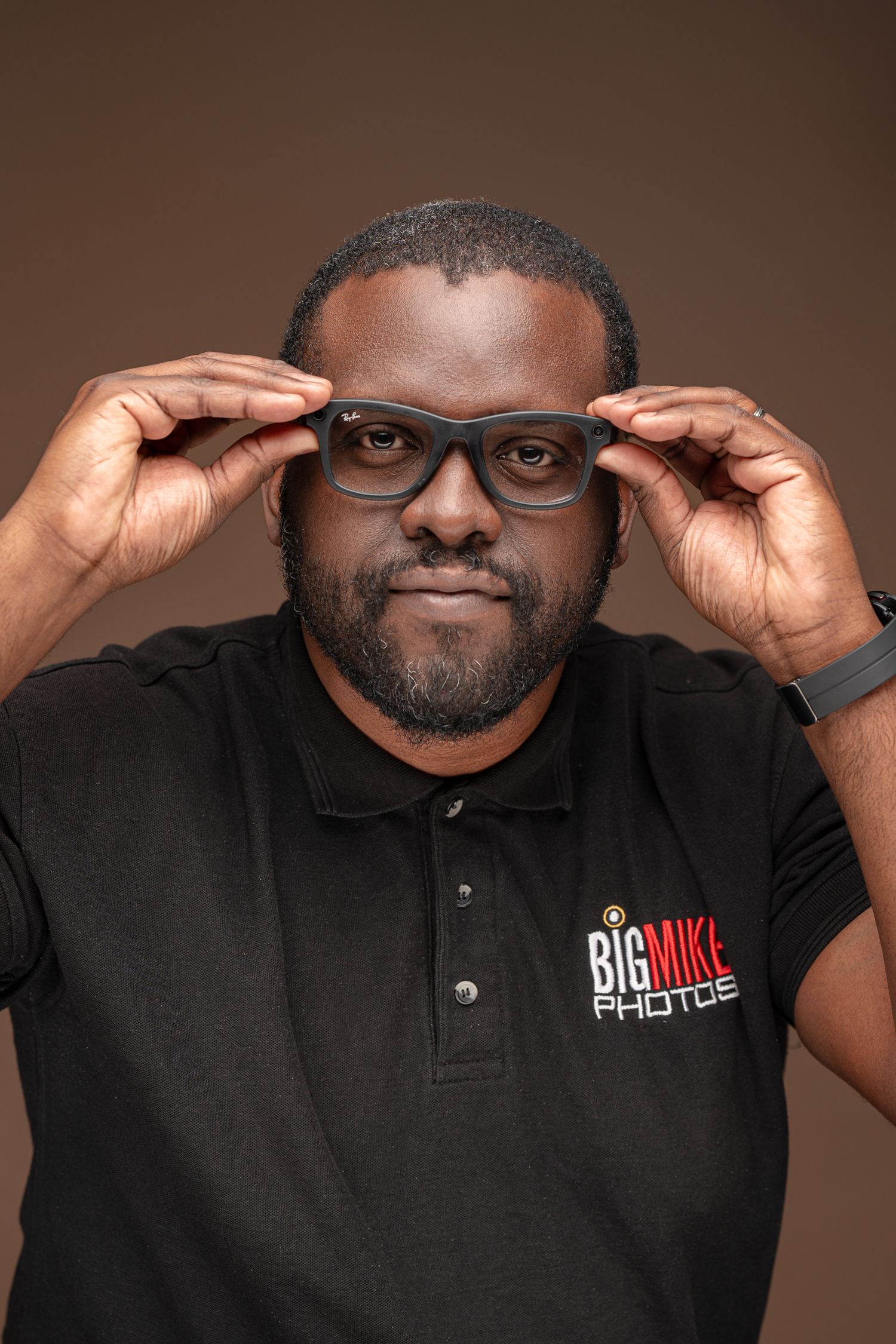 Photographer in glasses and branded polo adjusting eyewear while smiling at camera.