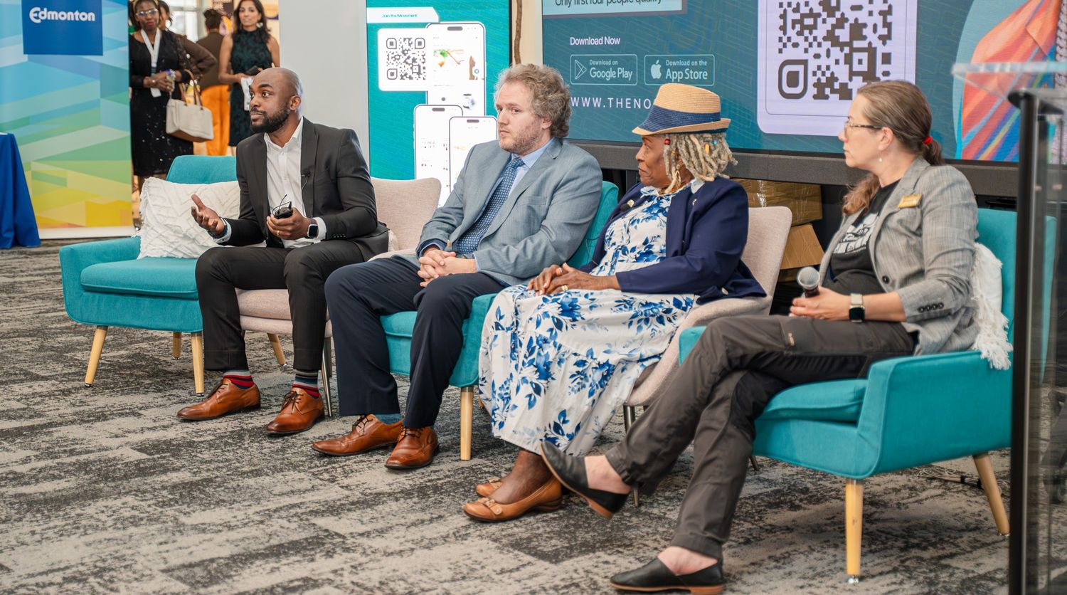 Panel discussion with speakers seated in blue chairs on carpeted stage.