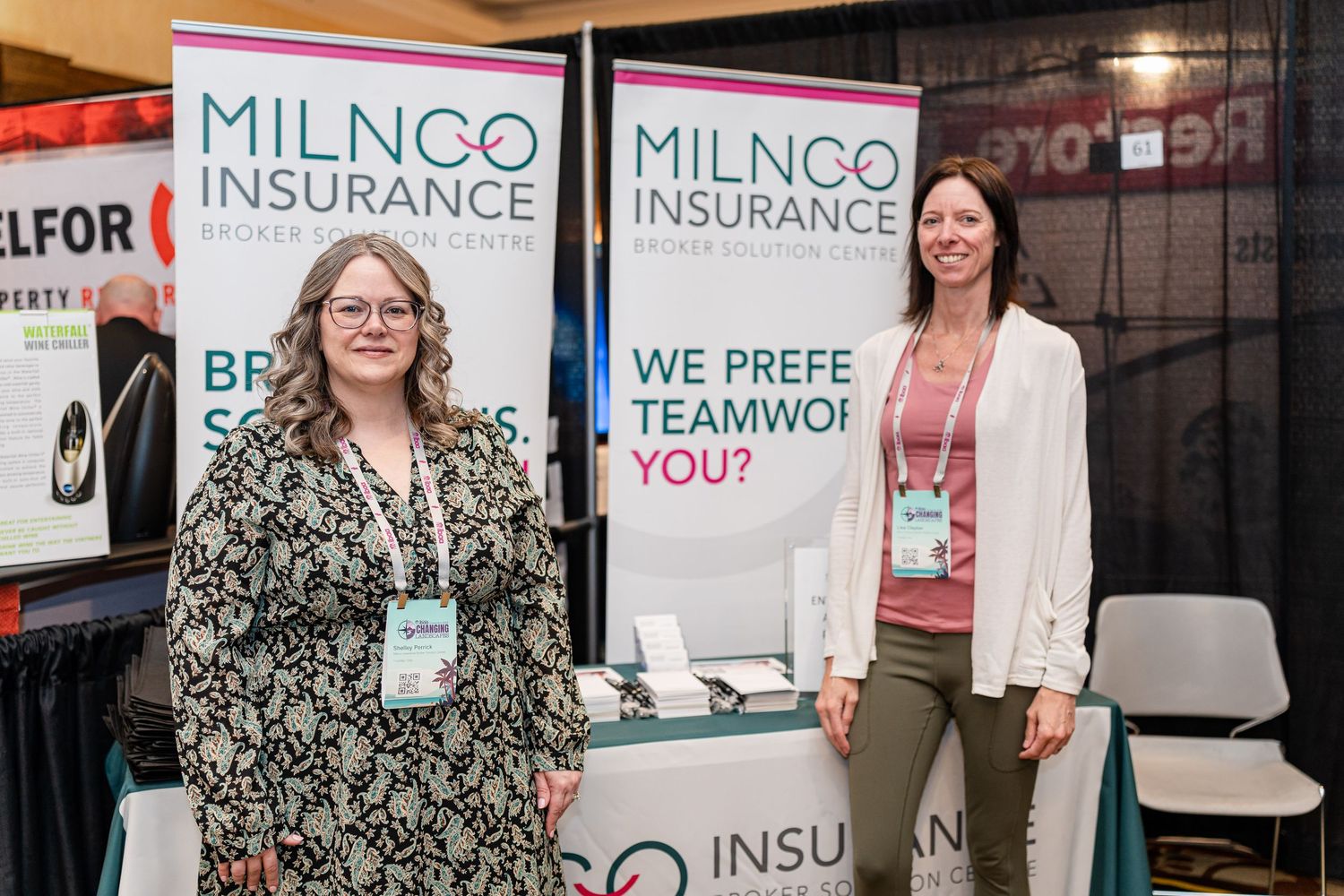 Two representatives stand at the Milnco Insurance booth at a business exhibition.