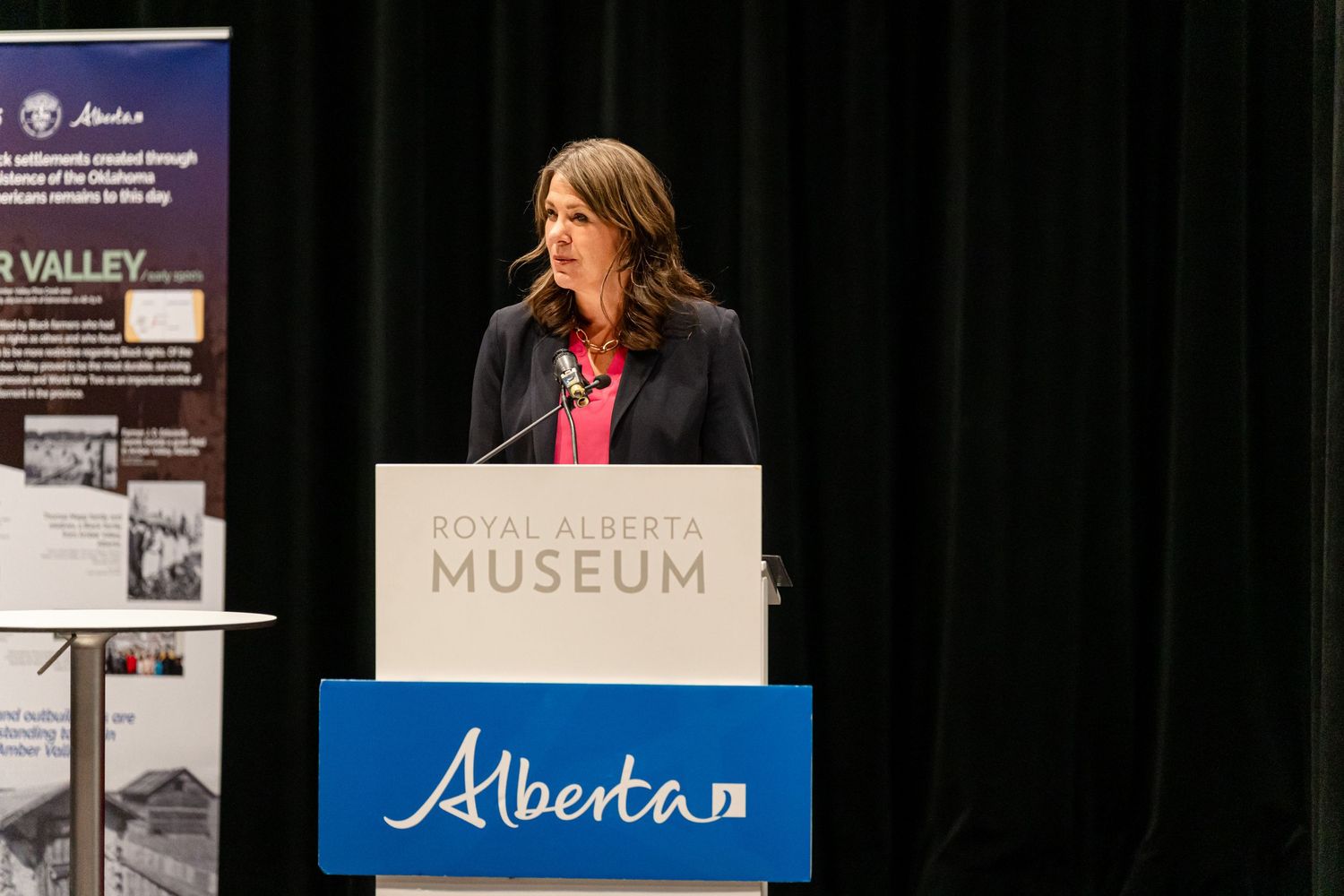 Presenter speaking at Royal Alberta Museum podium with blue Alberta banner displayed.
