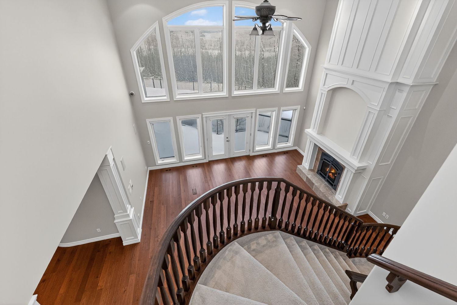 Elegant two-story foyer with curved staircase, hardwood floors, tall windows, built-in shelving, and a fireplace.