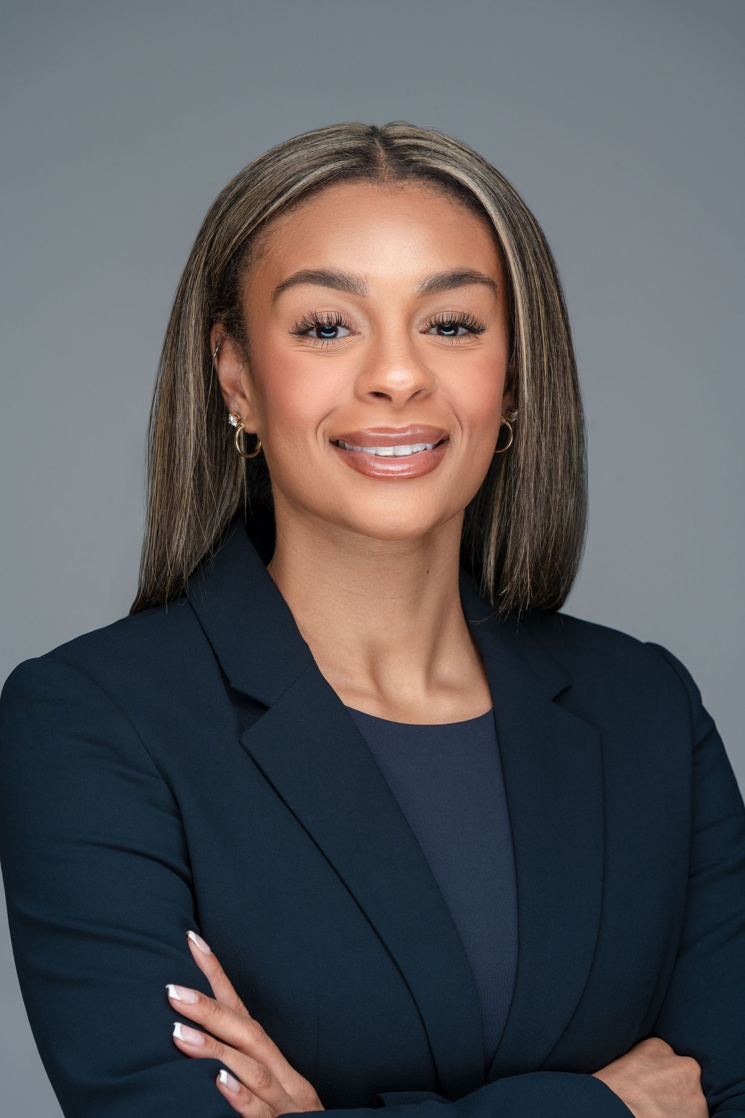 Professional studio portrait of a young professional in a dark blazer against a gray background.