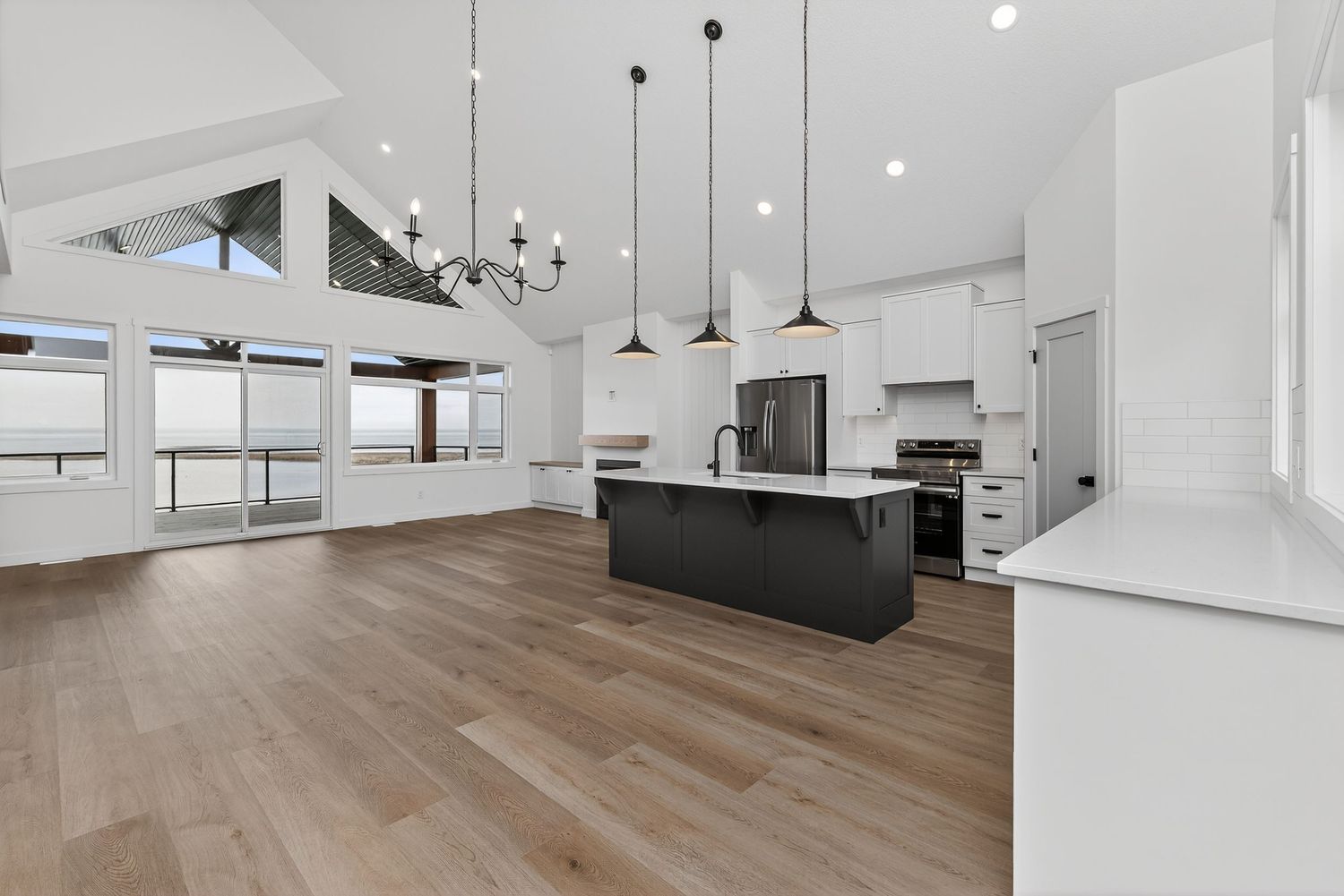 Modern open-concept kitchen with black island, white cabinets, pendant lights, vaulted ceilings, and hardwood floors.