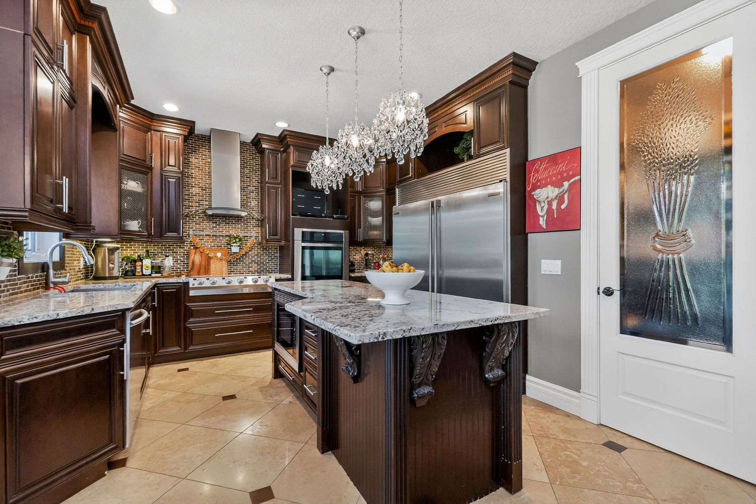Luxury kitchen with dark wood cabinets, granite island, stainless steel appliances, and elegant crystal chandelier lighting.