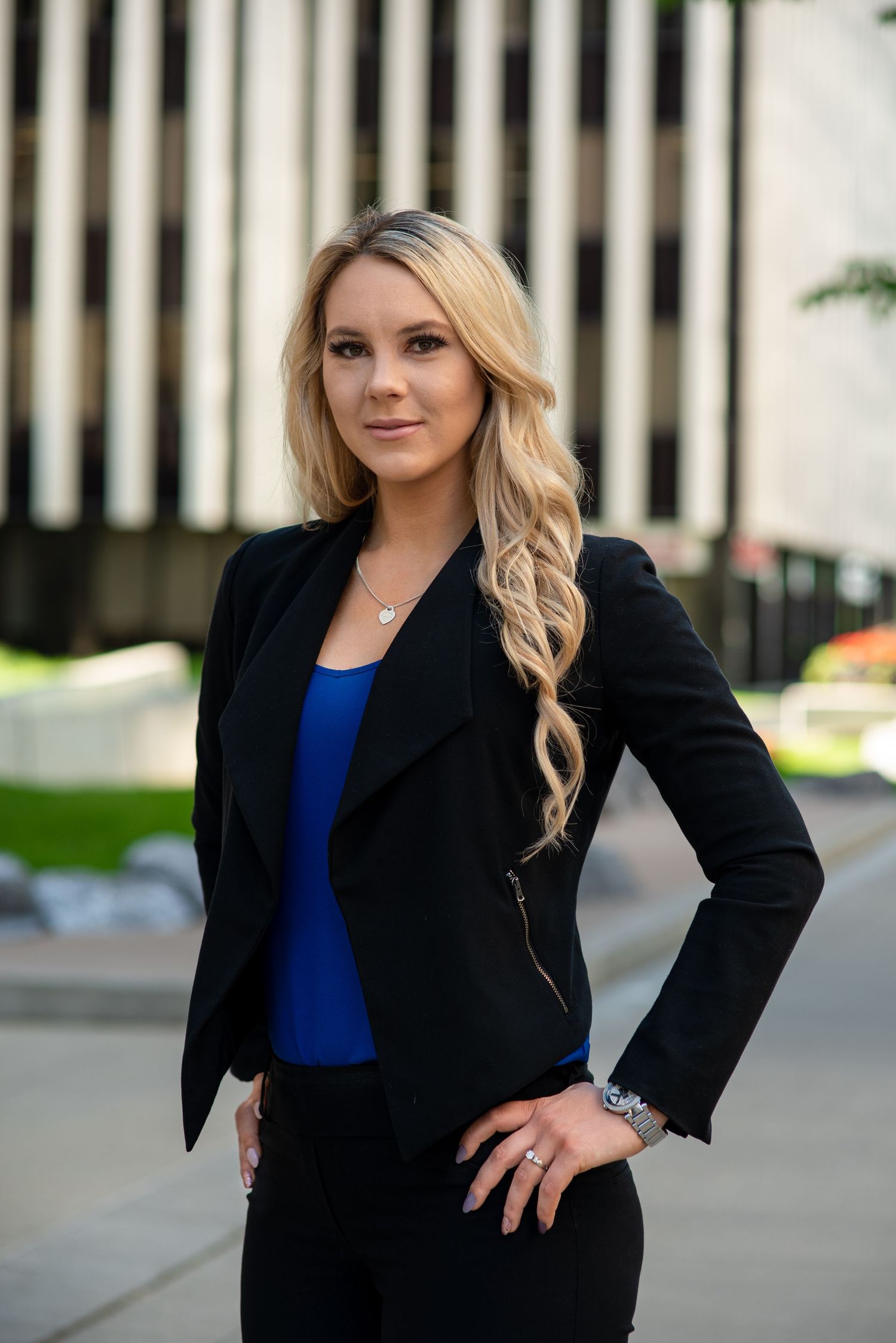 Professional business portrait in black blazer and blue top against modern architectural background.