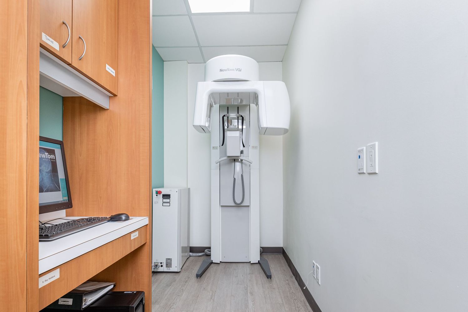 Dental X-ray machine in a narrow hallway with wooden cabinets and gray flooring.