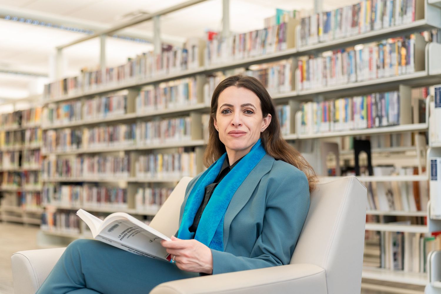 Professional woman in blue blazer reads book in library setting.