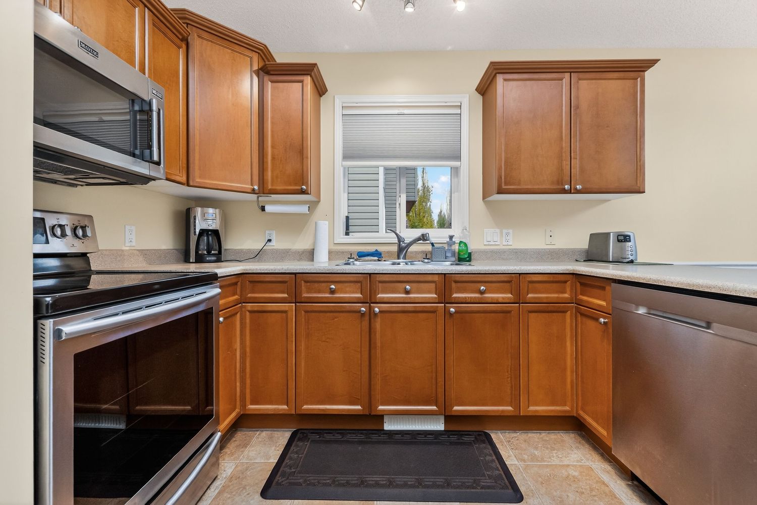 Modern kitchen with honey oak cabinets, stainless steel appliances, and tile flooring surrounding a central sink window.