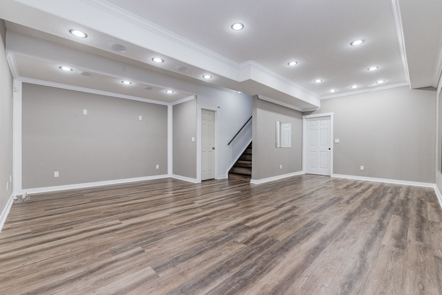 Spacious finished basement with gray walls, hardwood floors, recessed lighting, and staircase leading upstairs.
